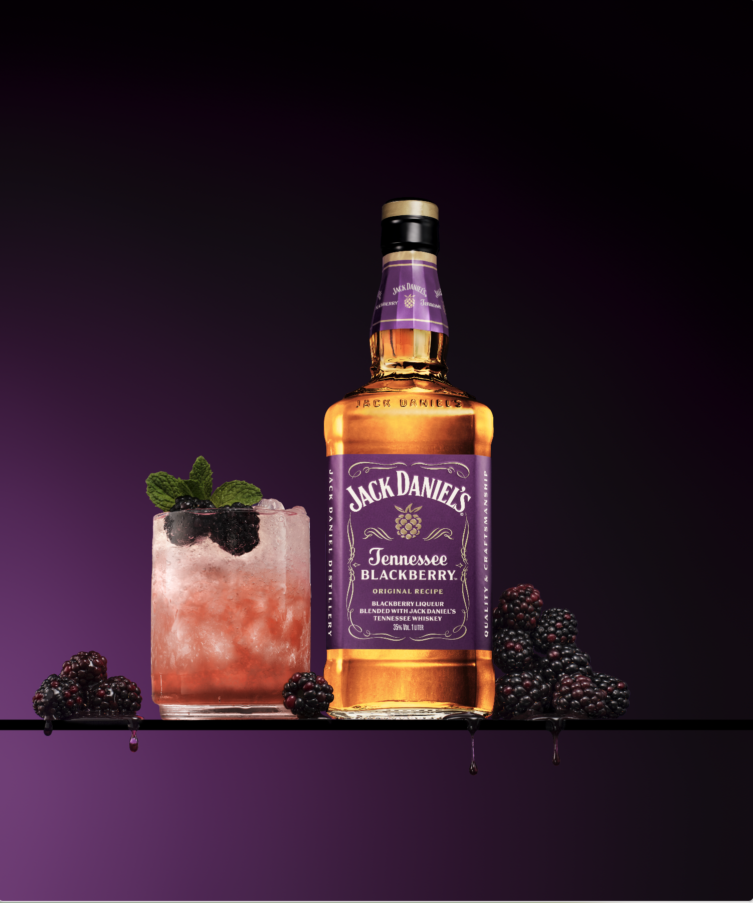 A bottle of Jack Daniel's Tennessee Blackberry whiskey next to a blackberry cocktail with fresh blackberries and mint leaves on a reflective surface with a dark purple background.