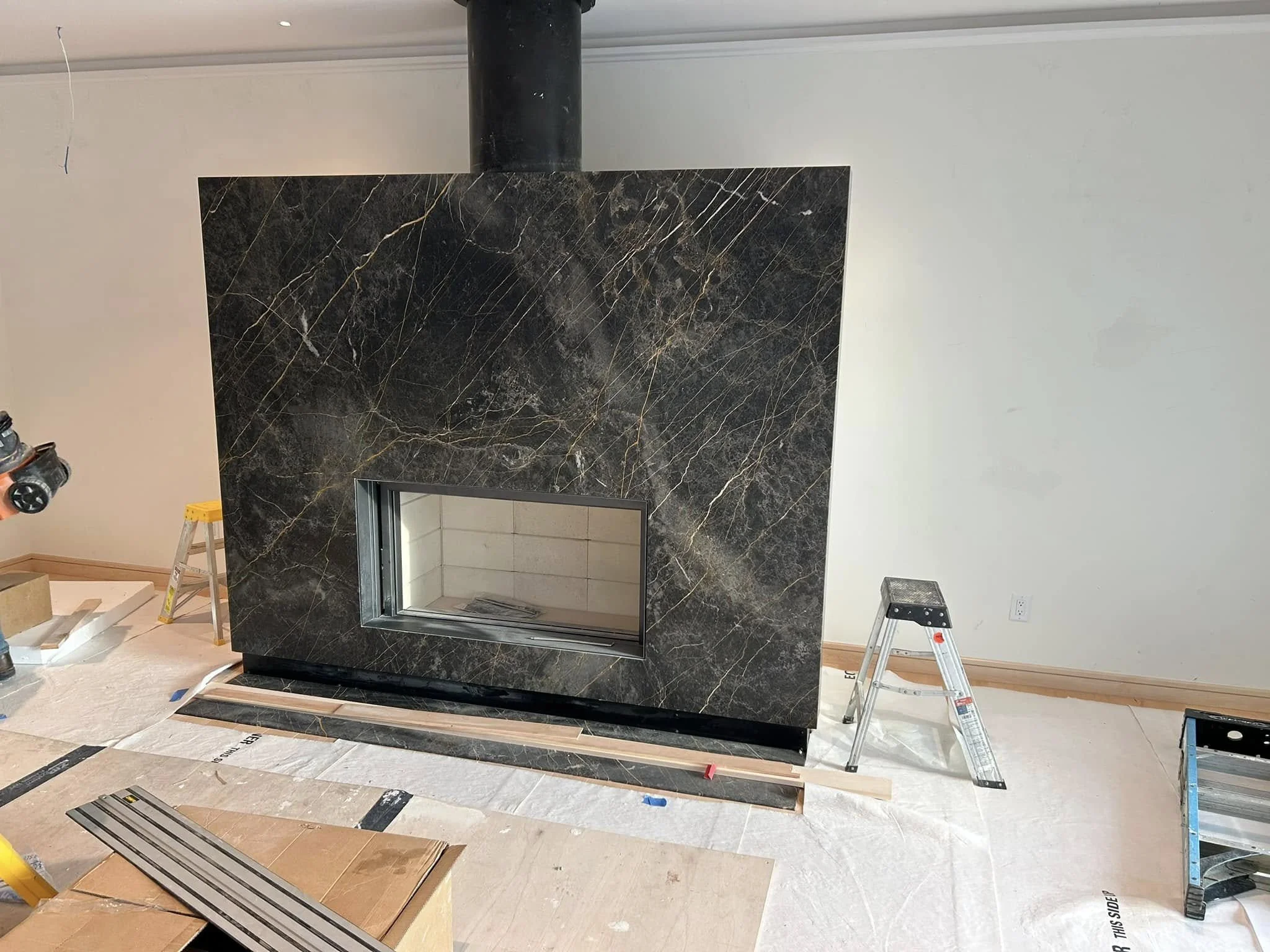 Modern fireplace with a black marble hearth surround under construction.