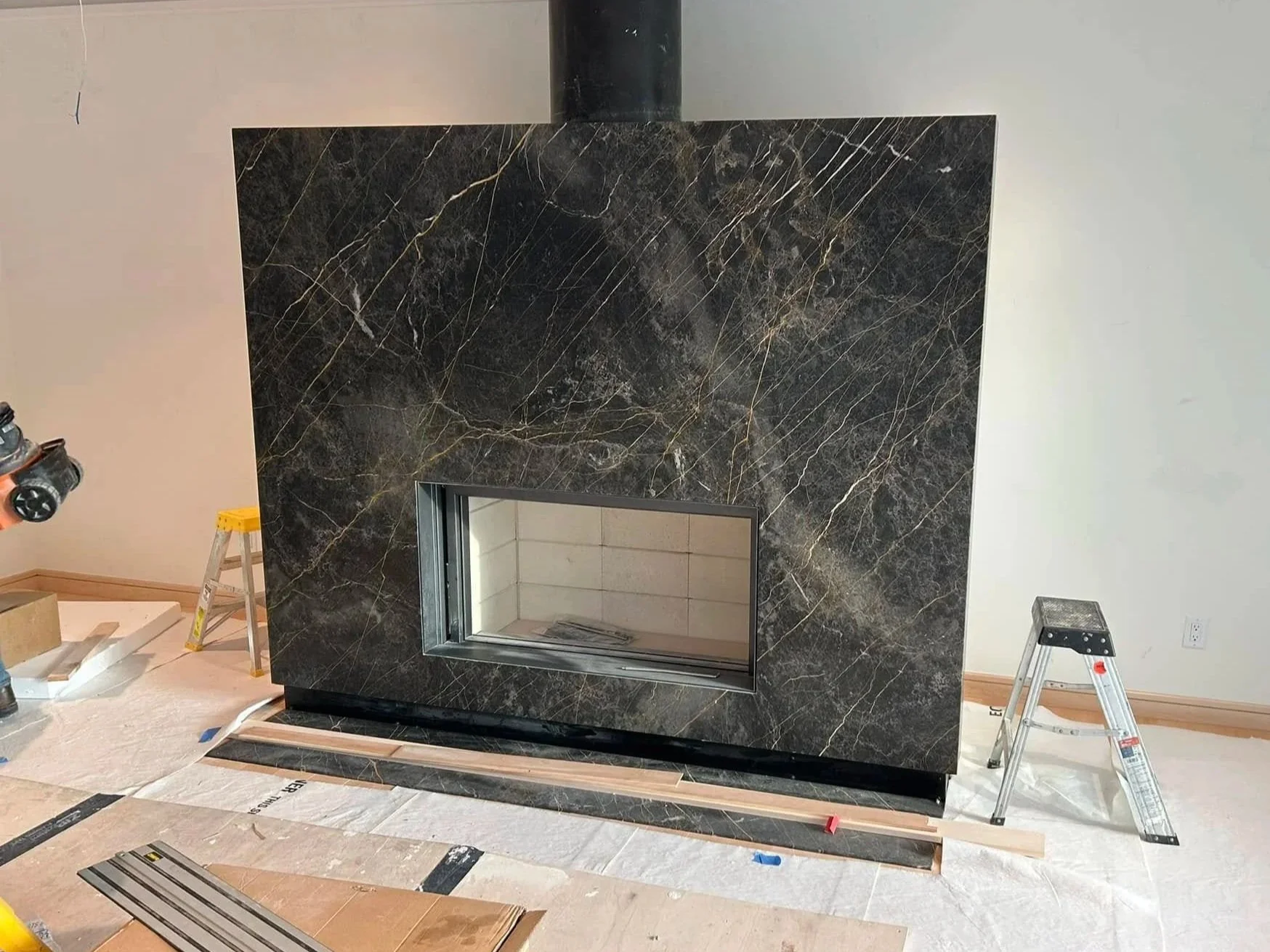 A black marble fireplace under construction, with parts of the building materials and ladders around it.