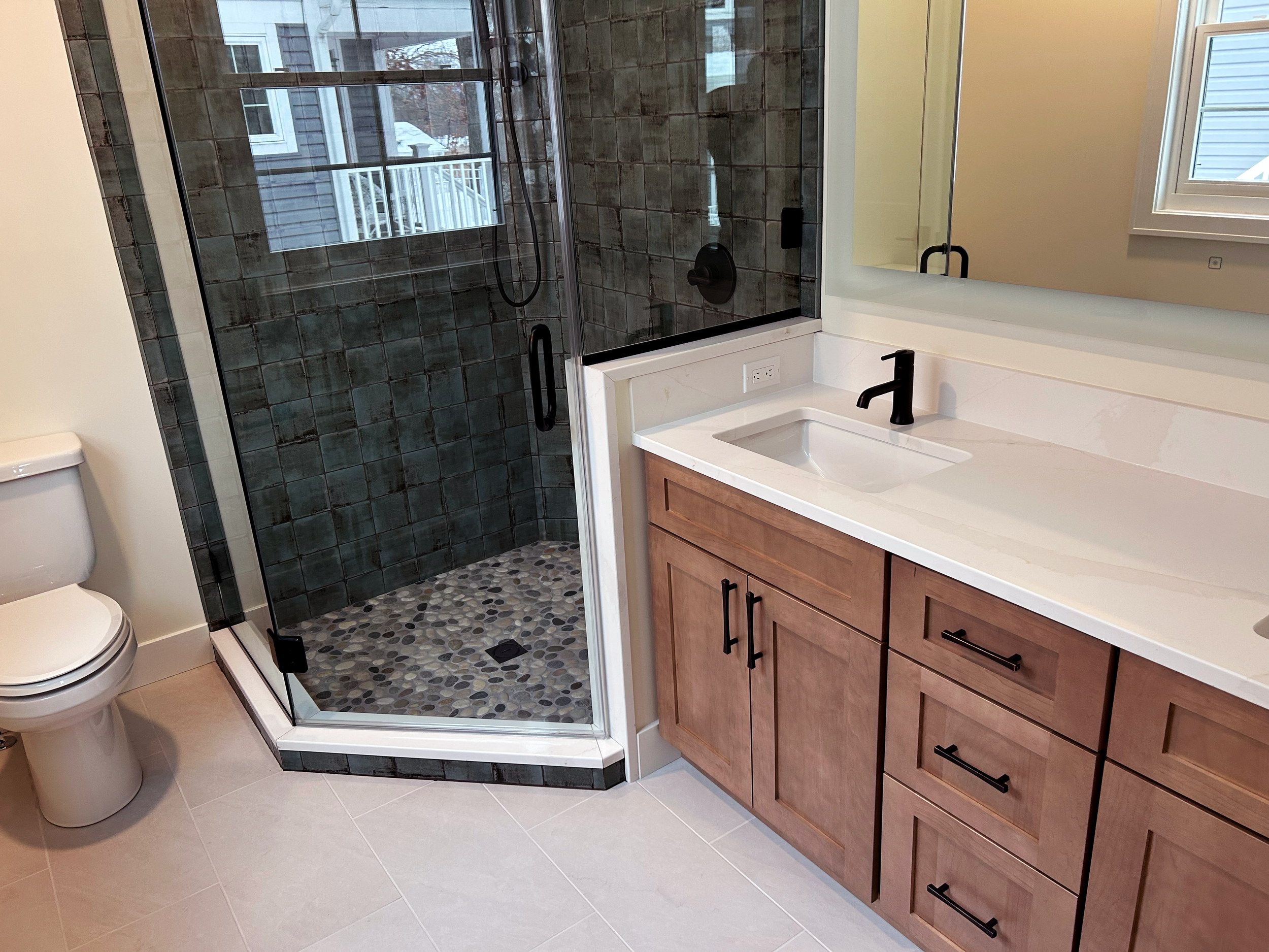 Modern bathroom with a glass shower enclosure, a white vanity with a sink and black faucet, a large mirror, toilet, and tiled floor.