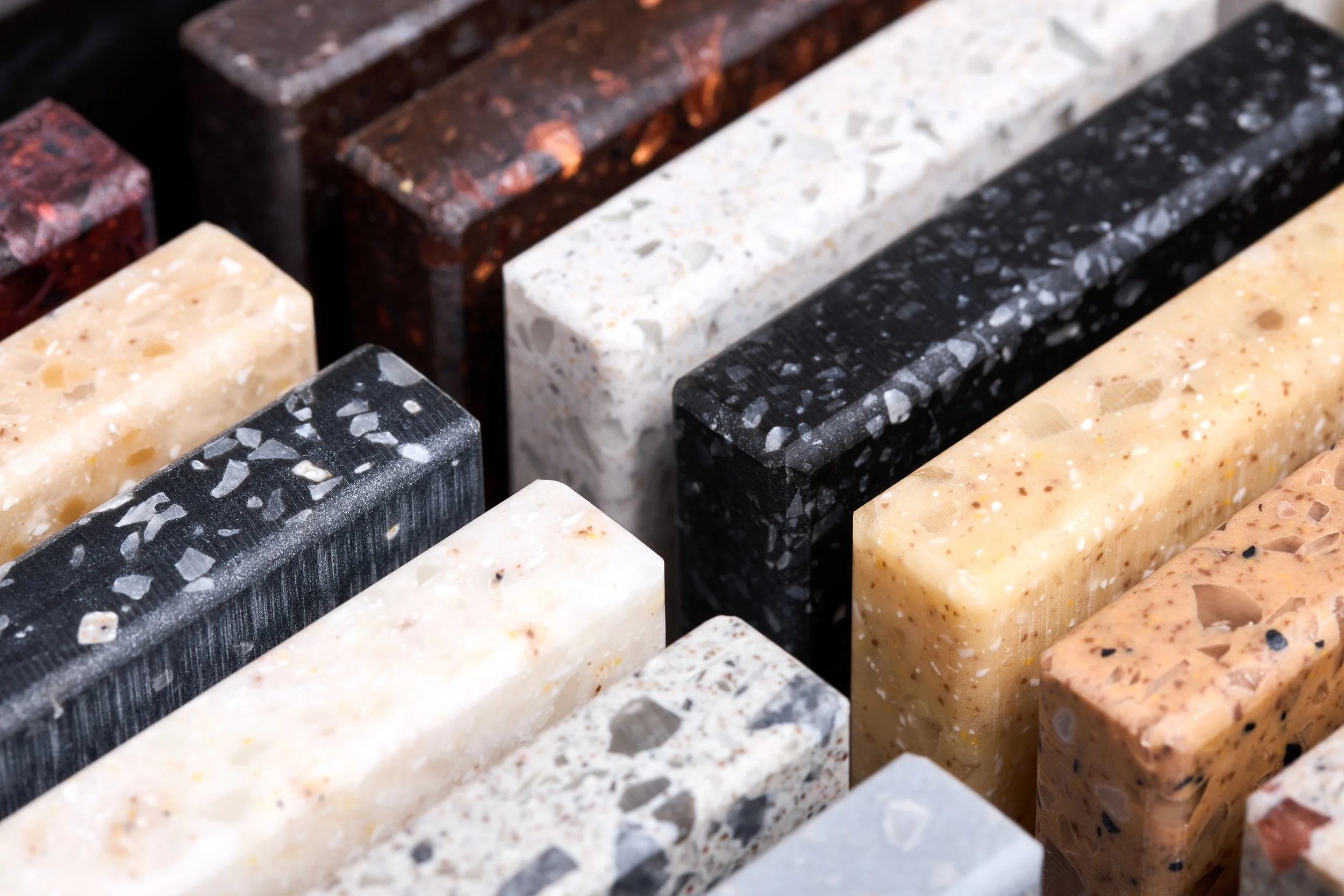 A collection of various colored granite and quartz stones arranged in rows.