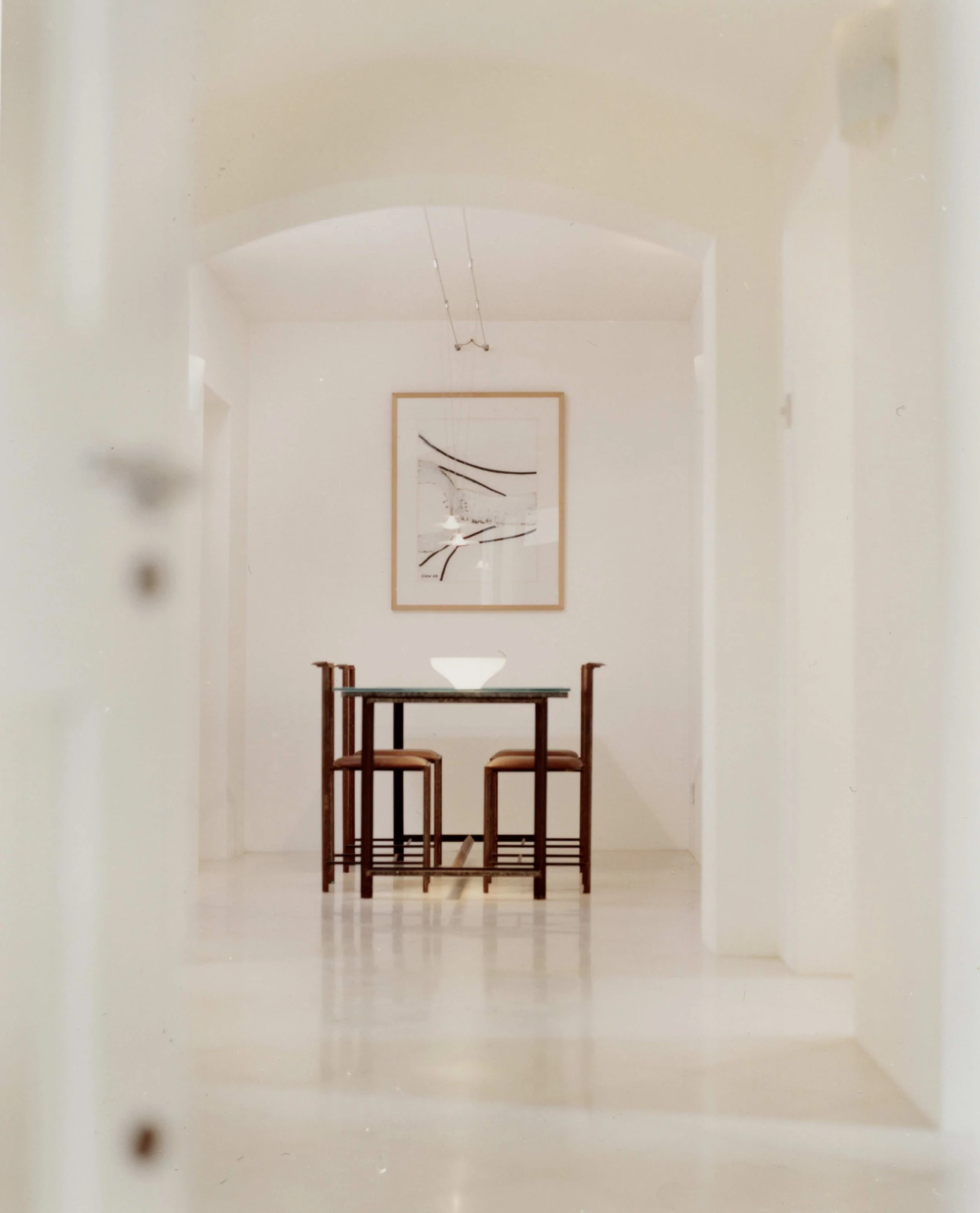 Minimalist hallway and dining area with a glass table and four chairs, and modern artwork in a period building in Clifton, Bristol