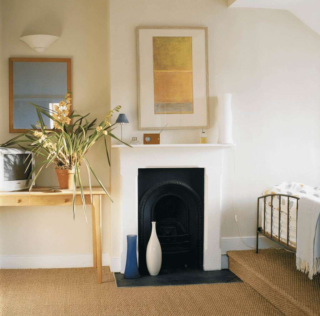 Attic room in Cotham, Bristol room with a white fireplace, framed artwork, a potted plant, vases, a mirror, a TV, and a crib with a white blanket.
