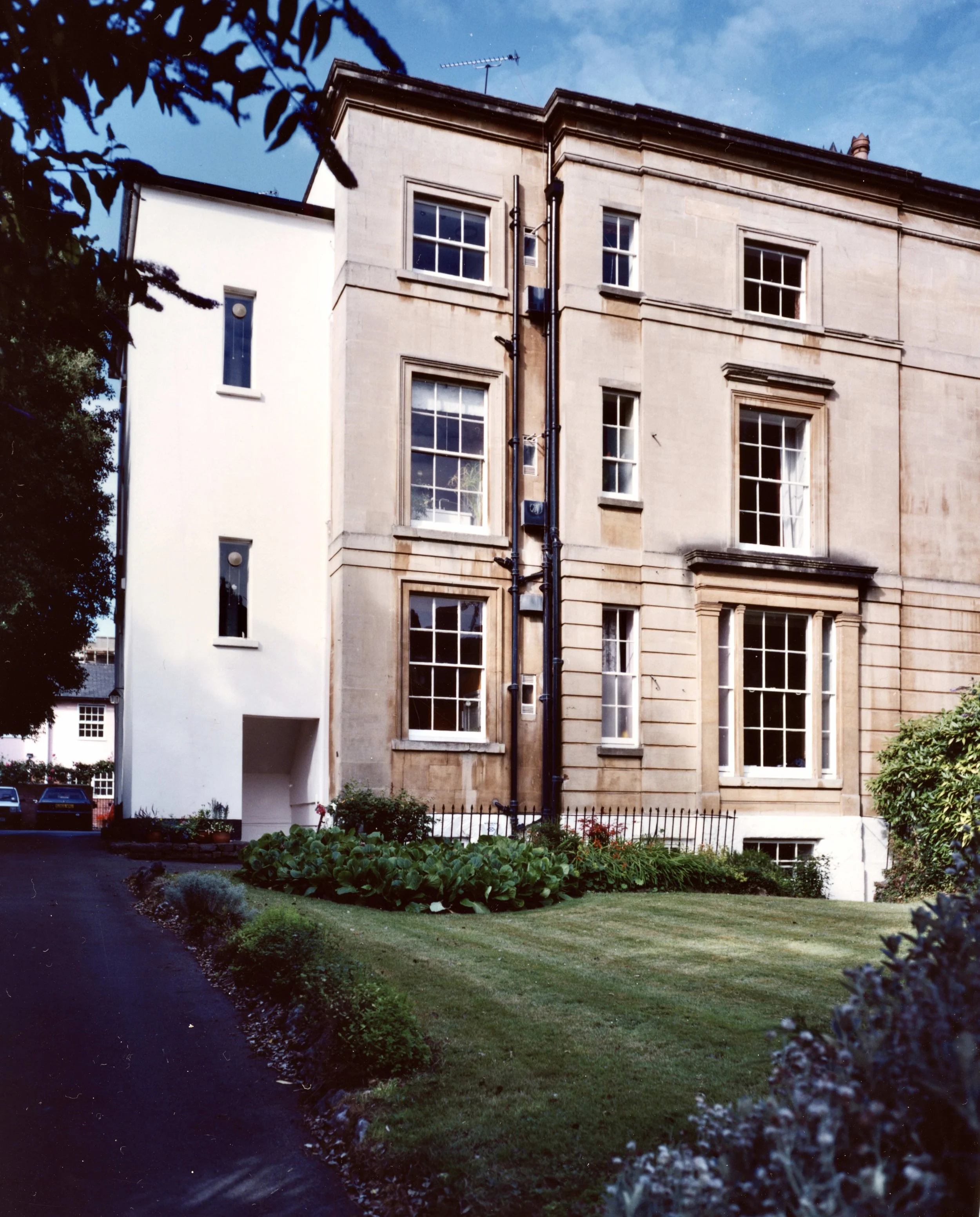 Front view of a Georgian-period home in Clifton, Bristol with large windows and a small garden with lush green grass and flowers in front.