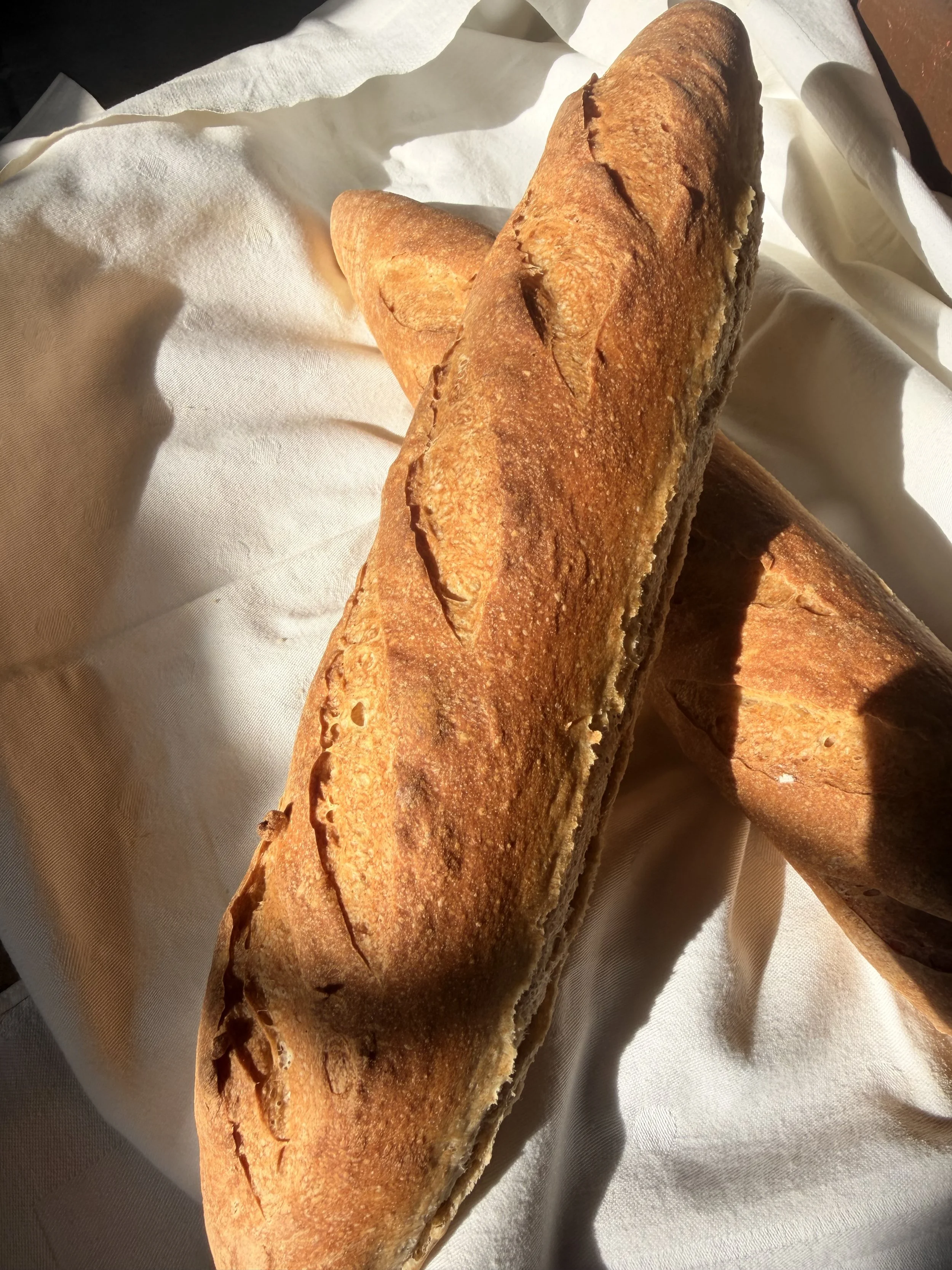 Two baguettes on a white cloth with sunlight casting shadows.