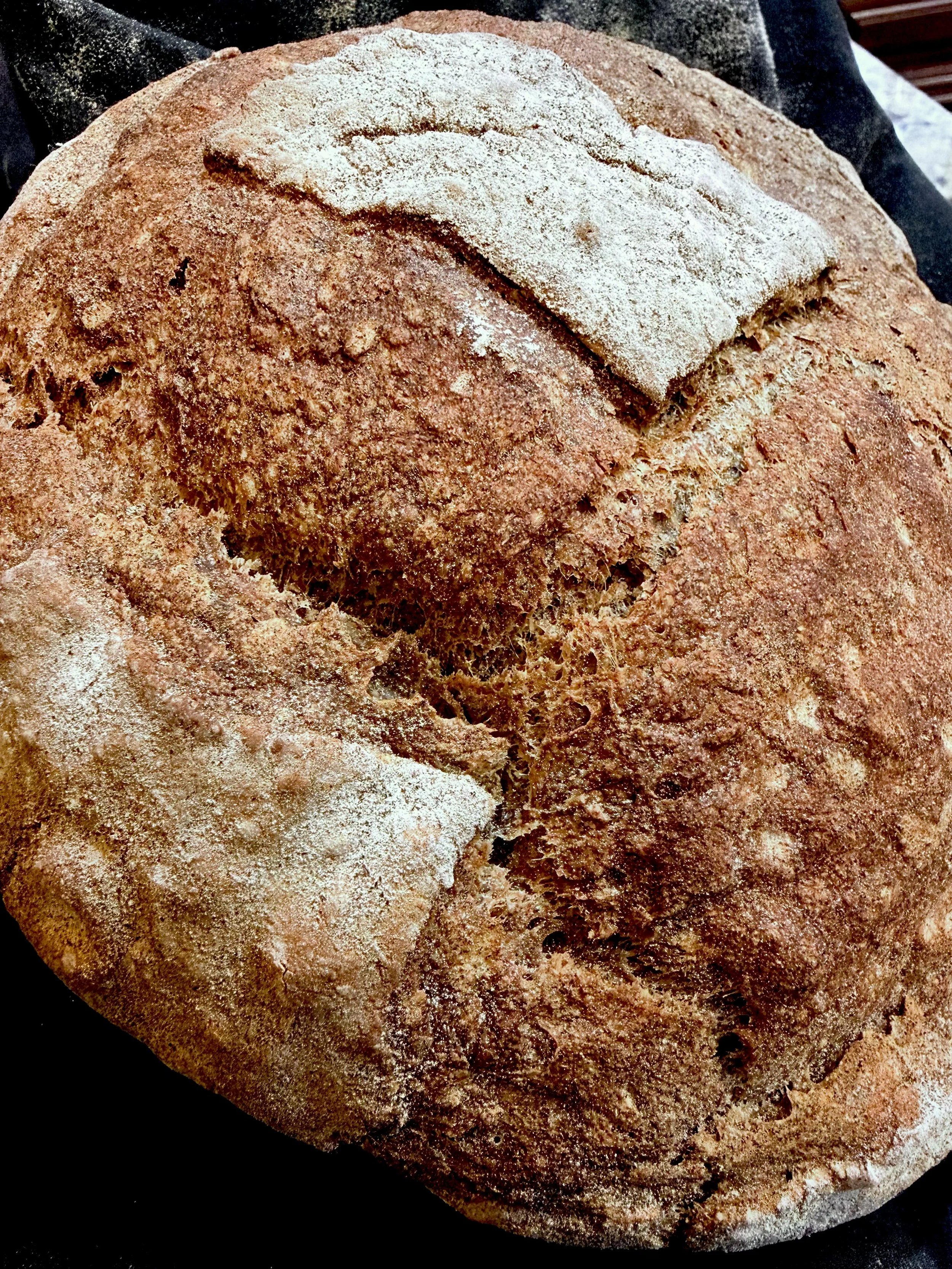 A large loaf of rustic bread with a dusting of flour and a slice cut from it.
