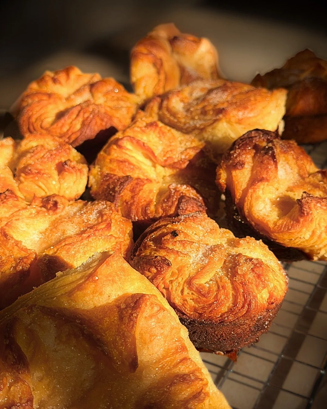 Close-up of golden-brown, crispy Kouign Amann Pastry with a slightly sugared surface resting on a cooling rack.