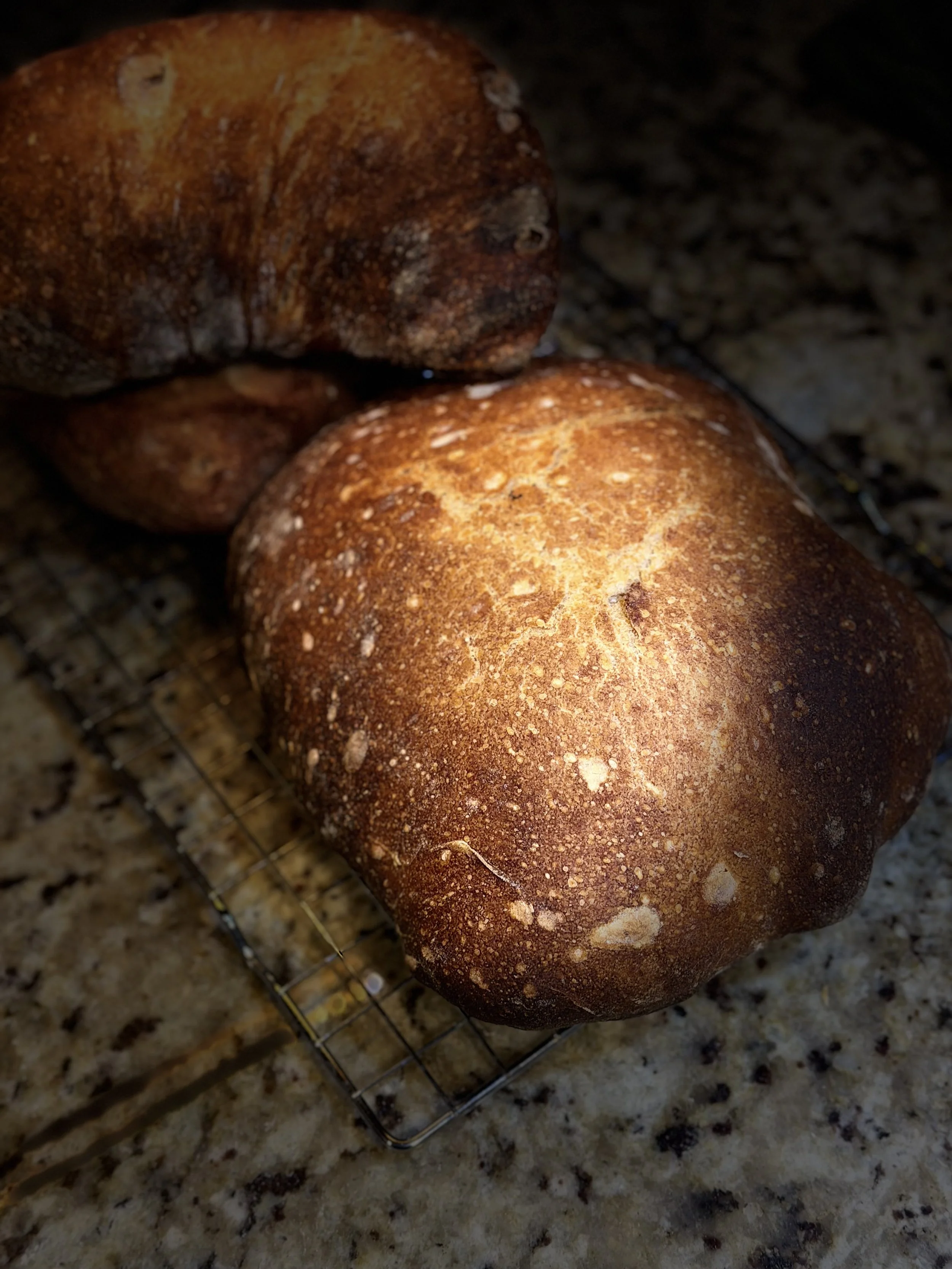 Two freshly baked bread loaves cooling on a wire rack on a granite countertop.