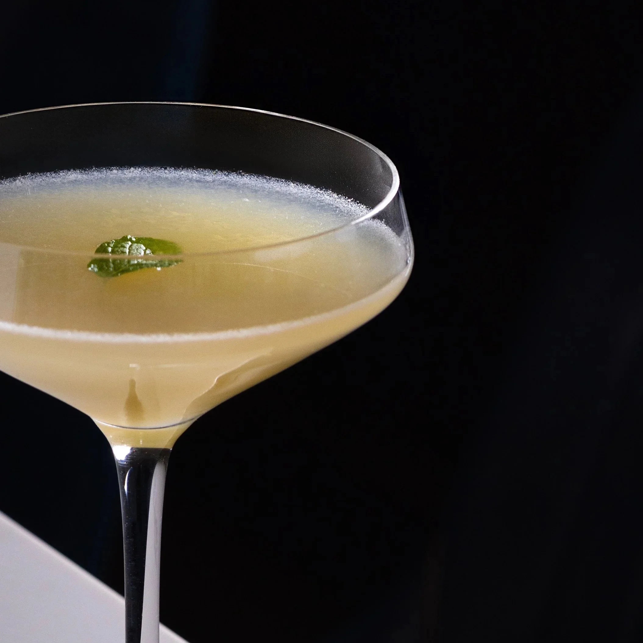 The Southside Shake cocktail in a coupe glass with a mint leaf garnish against a black background.