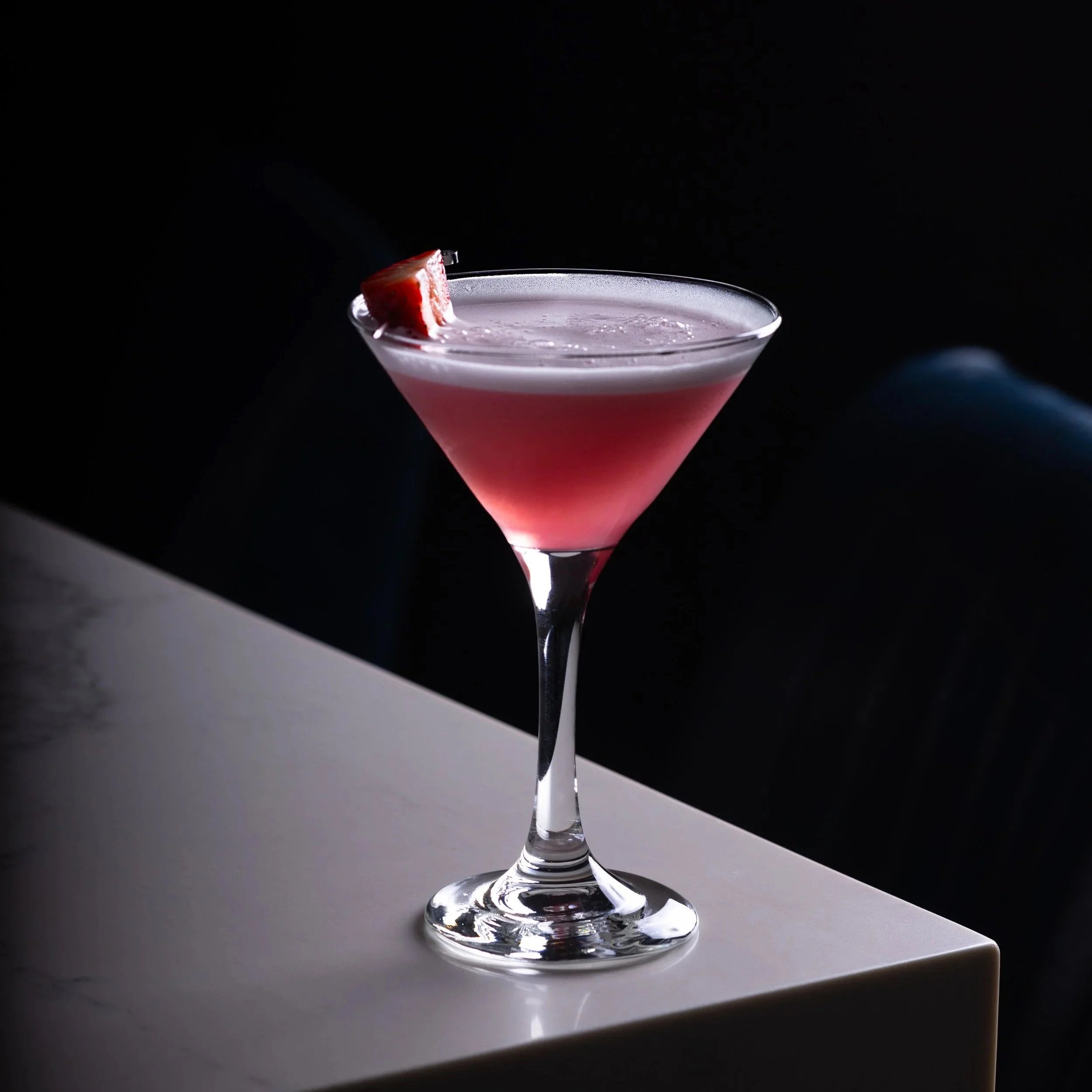 A pink gin cocktail in a martini glass garnished with a small slice of strawberry, placed on the white bar top of Southside Shake.