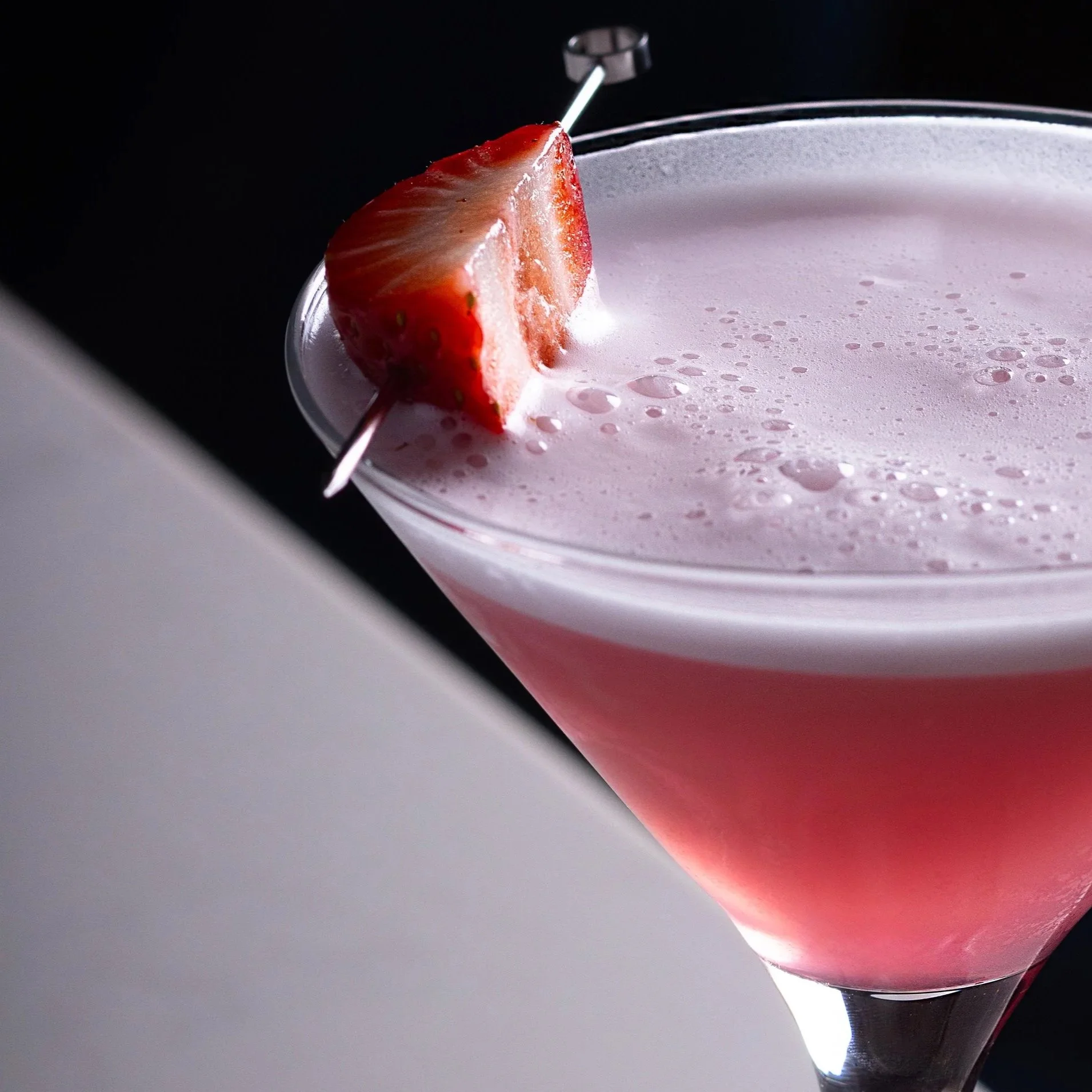 Close-up of a pink gin cocktail with frothy foam in a martini glass, garnished with a strawberry on a skewer at Southside Shake.