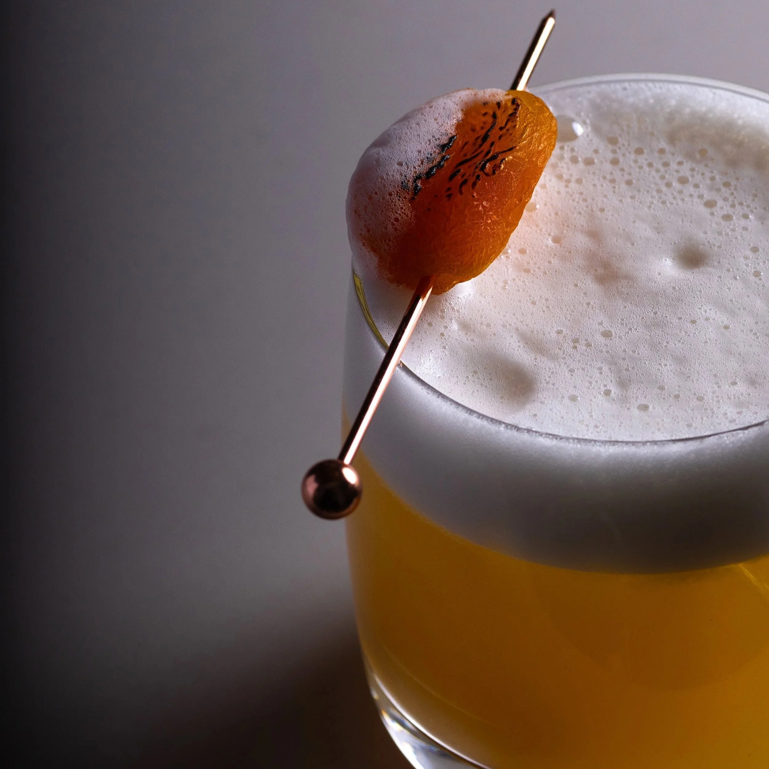Southside Shake's Apricot Sour, a  gin cocktail topped with foam, garnished with a slice of apricot fruit on a cocktail pick .