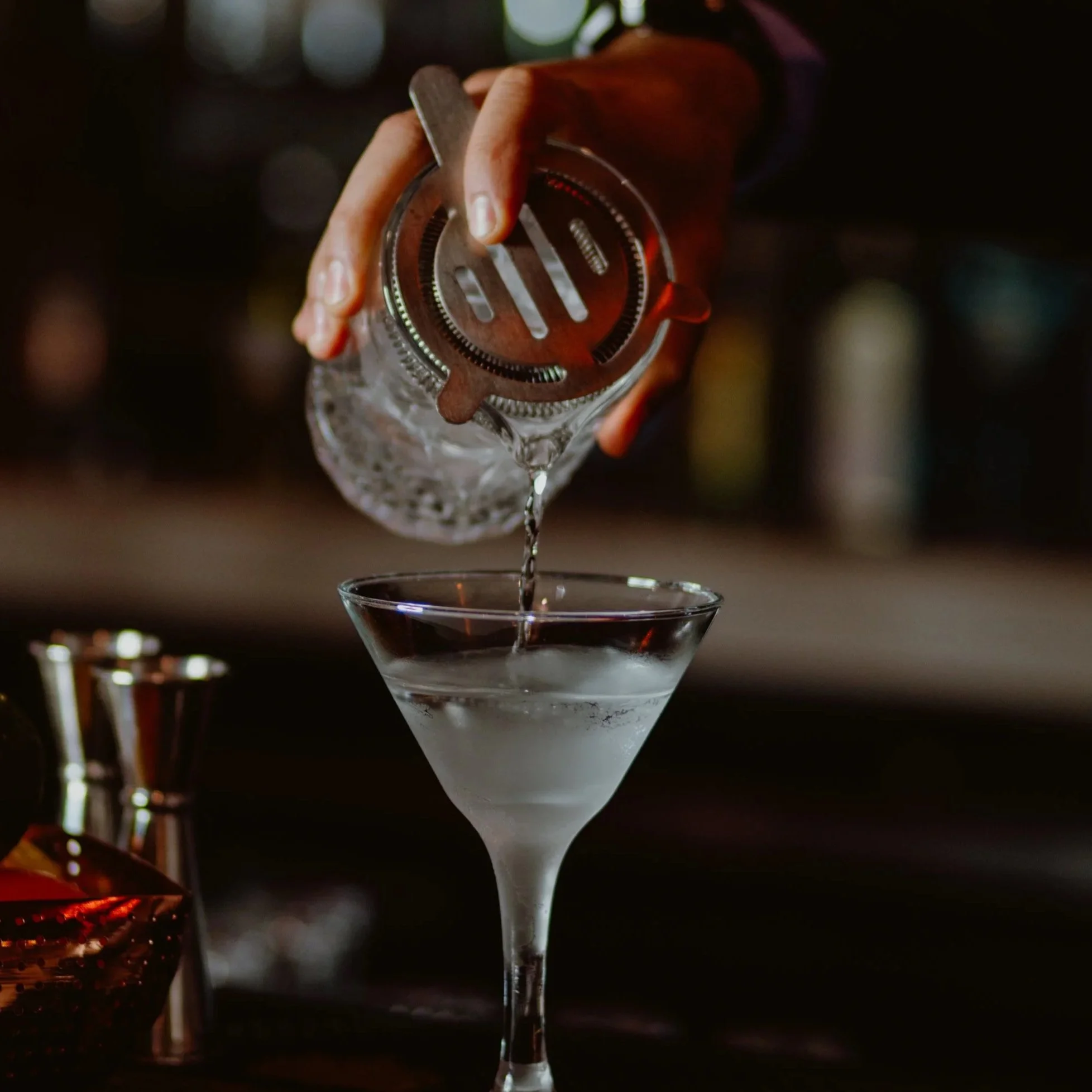 A bartender pours a clear gin liquid from a glass shaker into a martini glass at the Southside Shake bar.