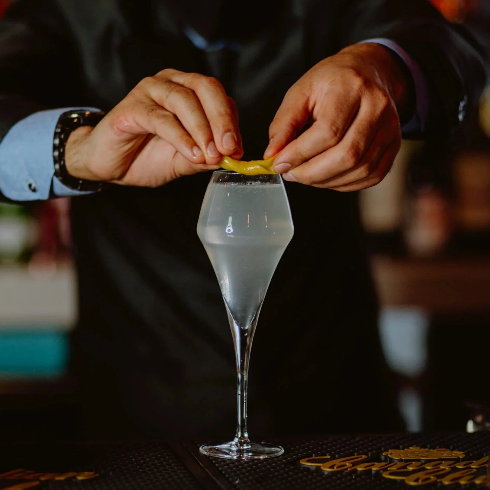 Two hands squeeze a yellow lemon half over a gin cocktail in a glass, with blurred background at Southside Shake.