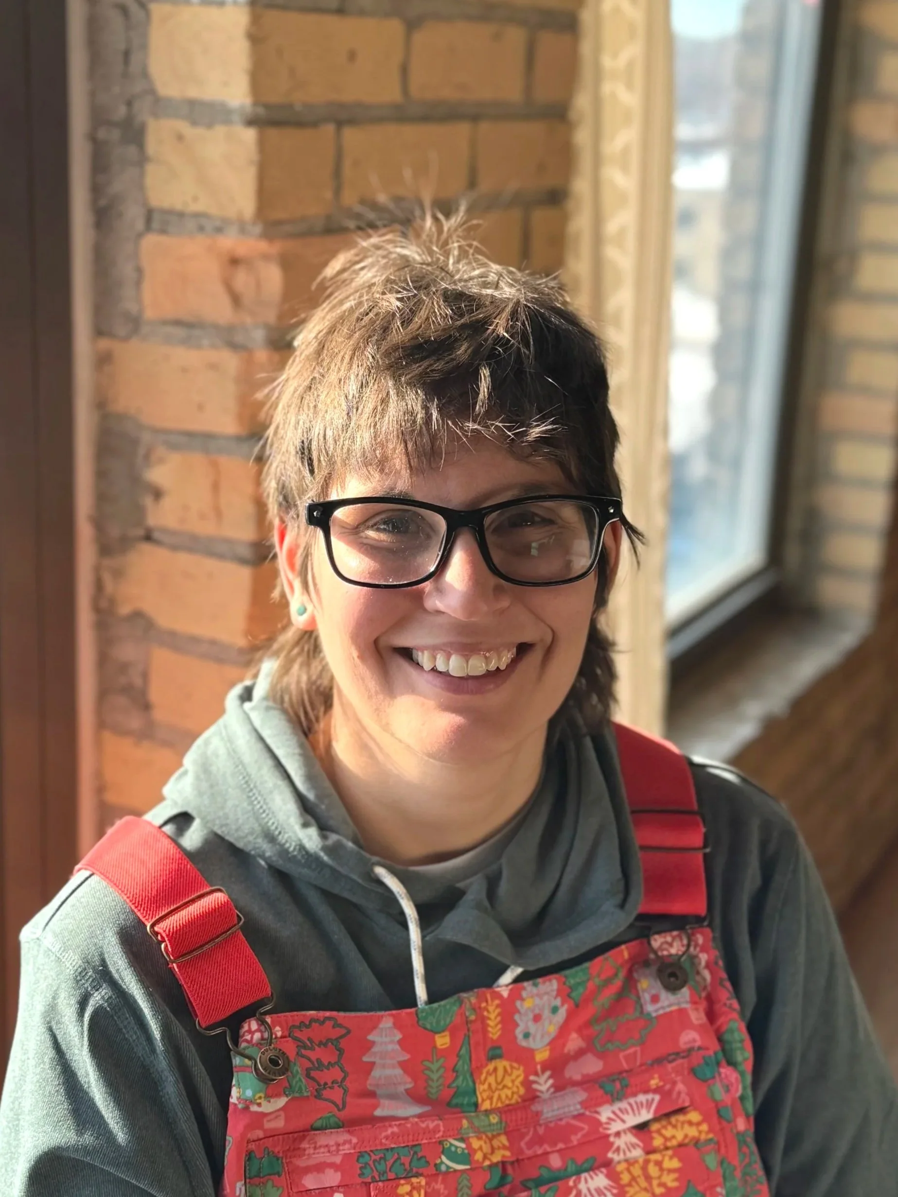 Headshot of an individual in front of a brick wall and windows.