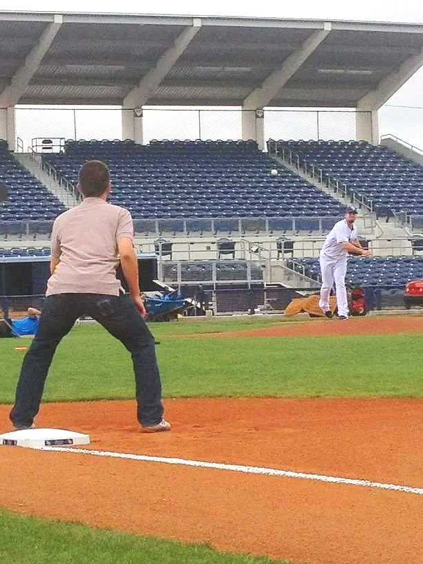 People practicing baseball on a field with empty stands in the background.