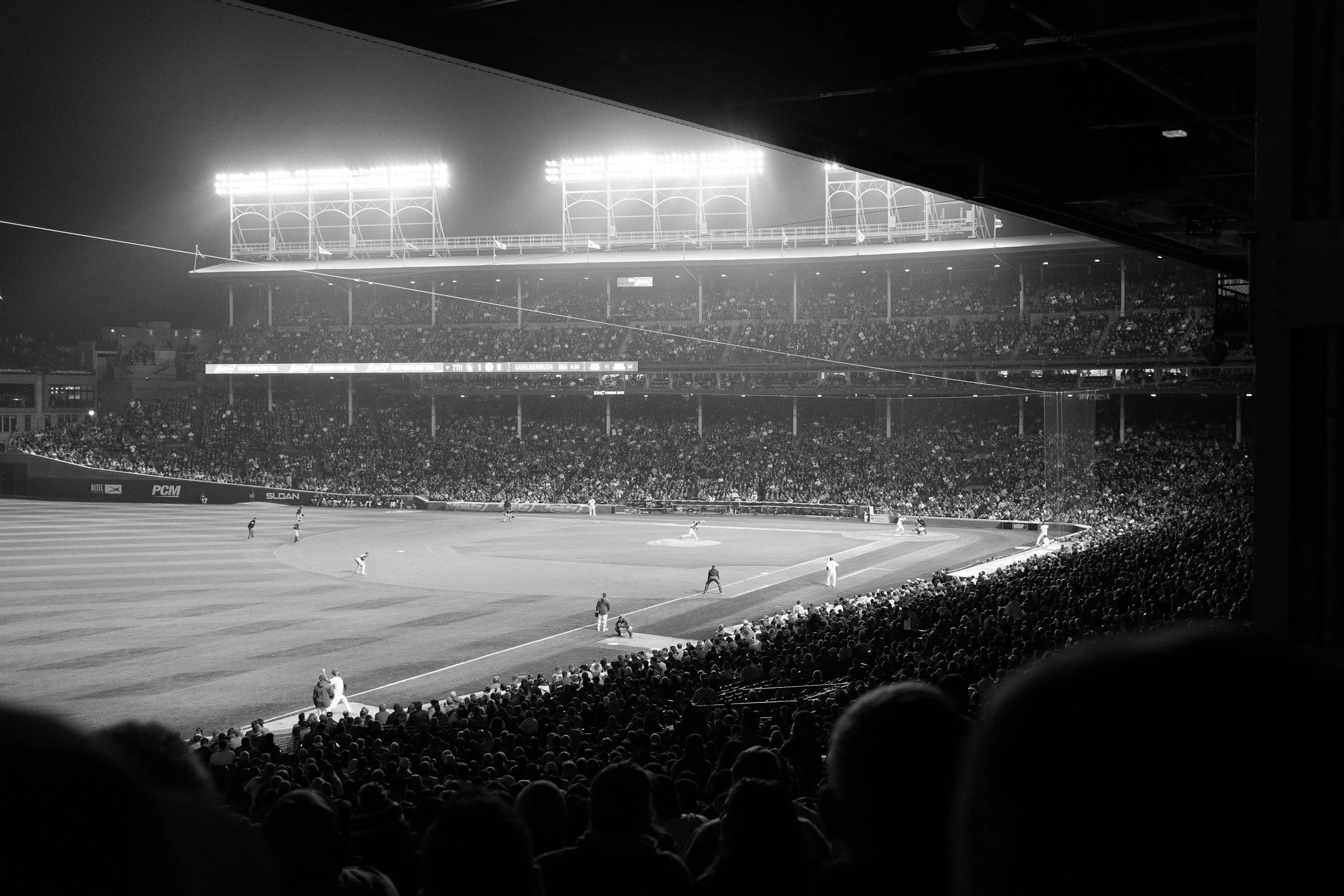Black and white photo of a baseball game at night in a packed stadium, viewed from the stands.