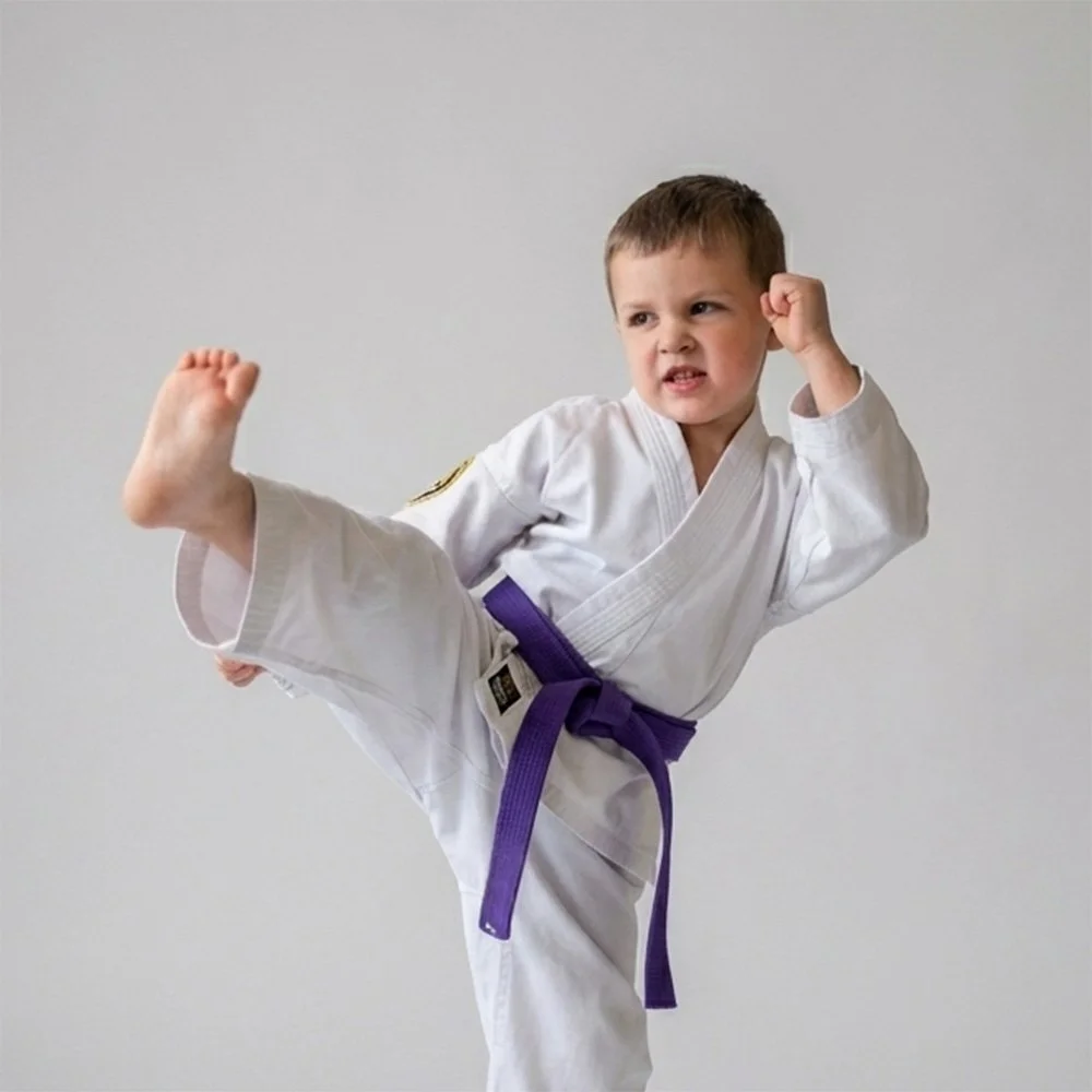 Young boy practicing martial arts in a karate uniform with a purple belt, performing a high kick and a fighting stance.