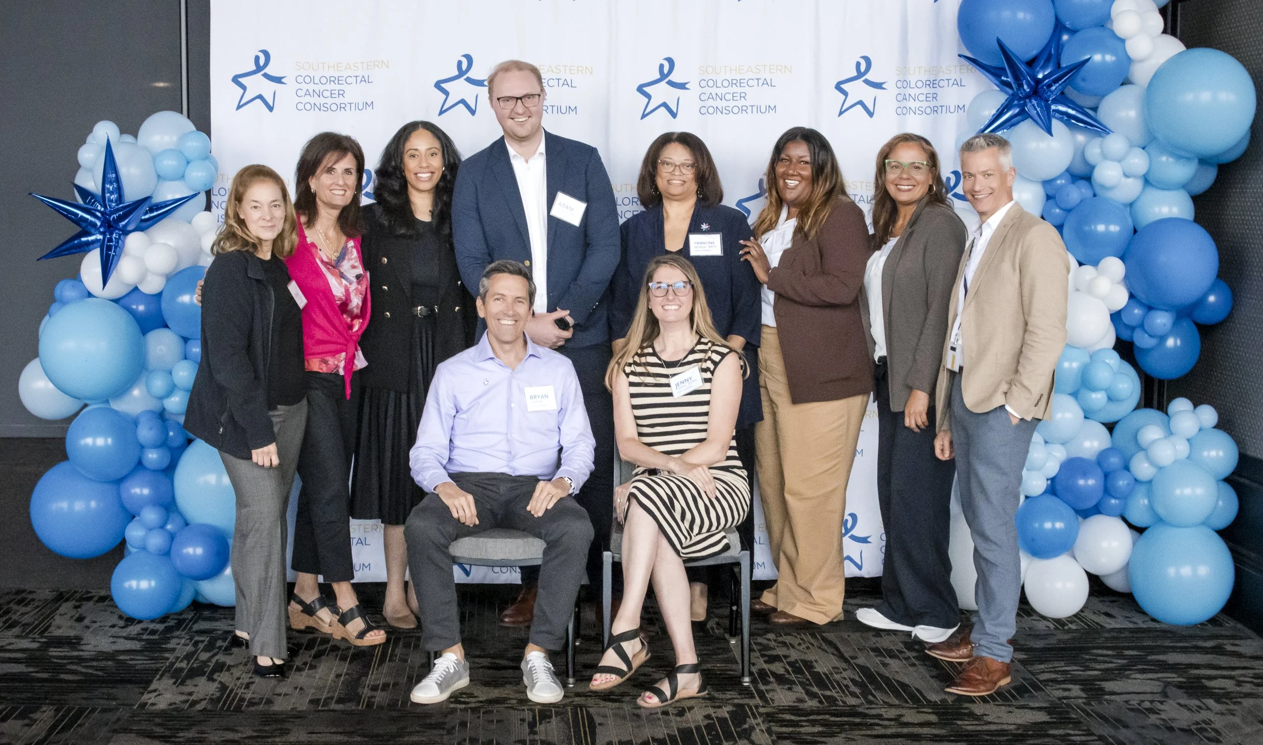 Group of ten people, five women and five men, posing for a photo at a Southeast Colorectal Cancer Consortium event, with balloon decorations in blue and white in the background.