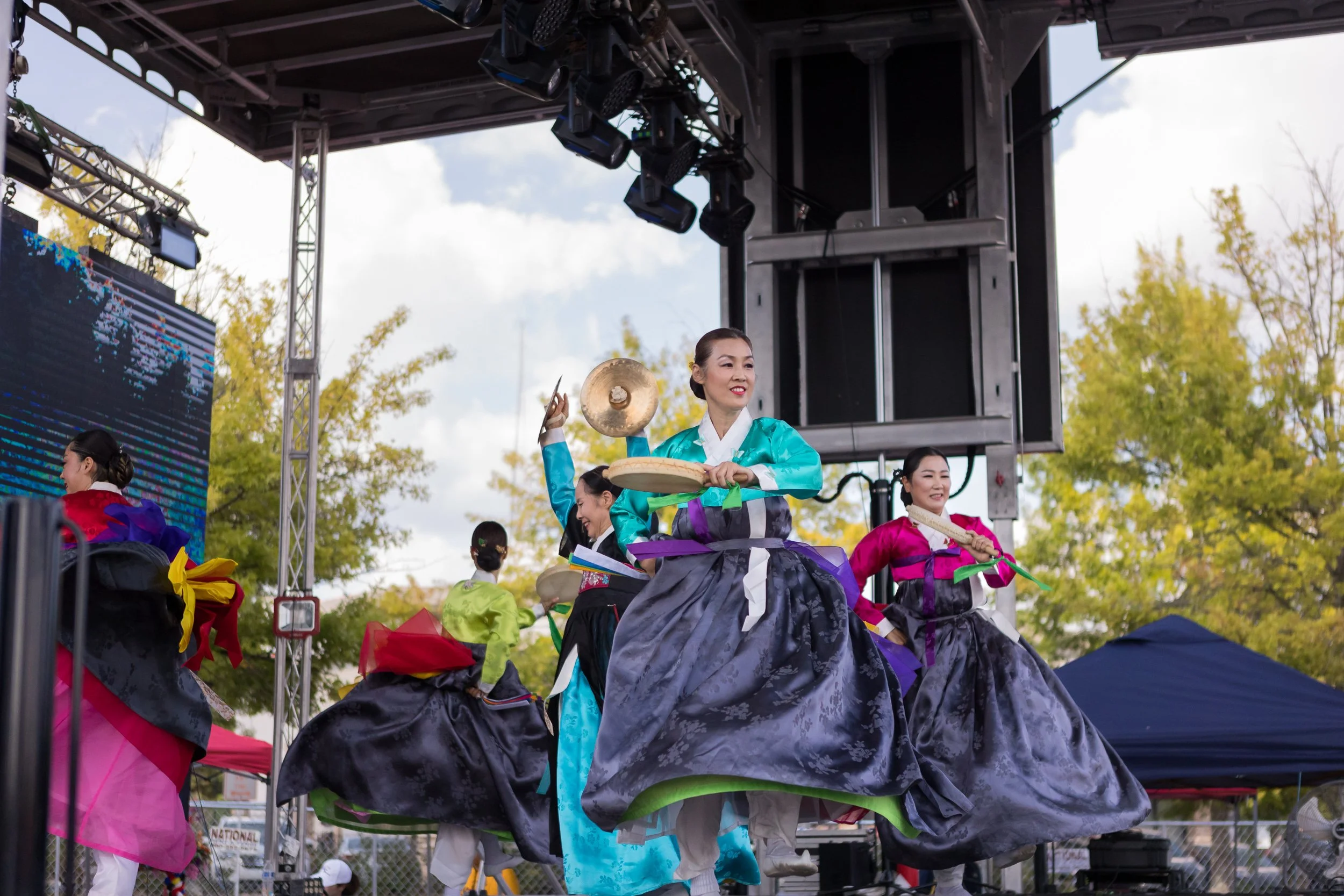 Women dressed in colorful traditional Korean hanbok performing a dance on an outdoor stage during a festival.