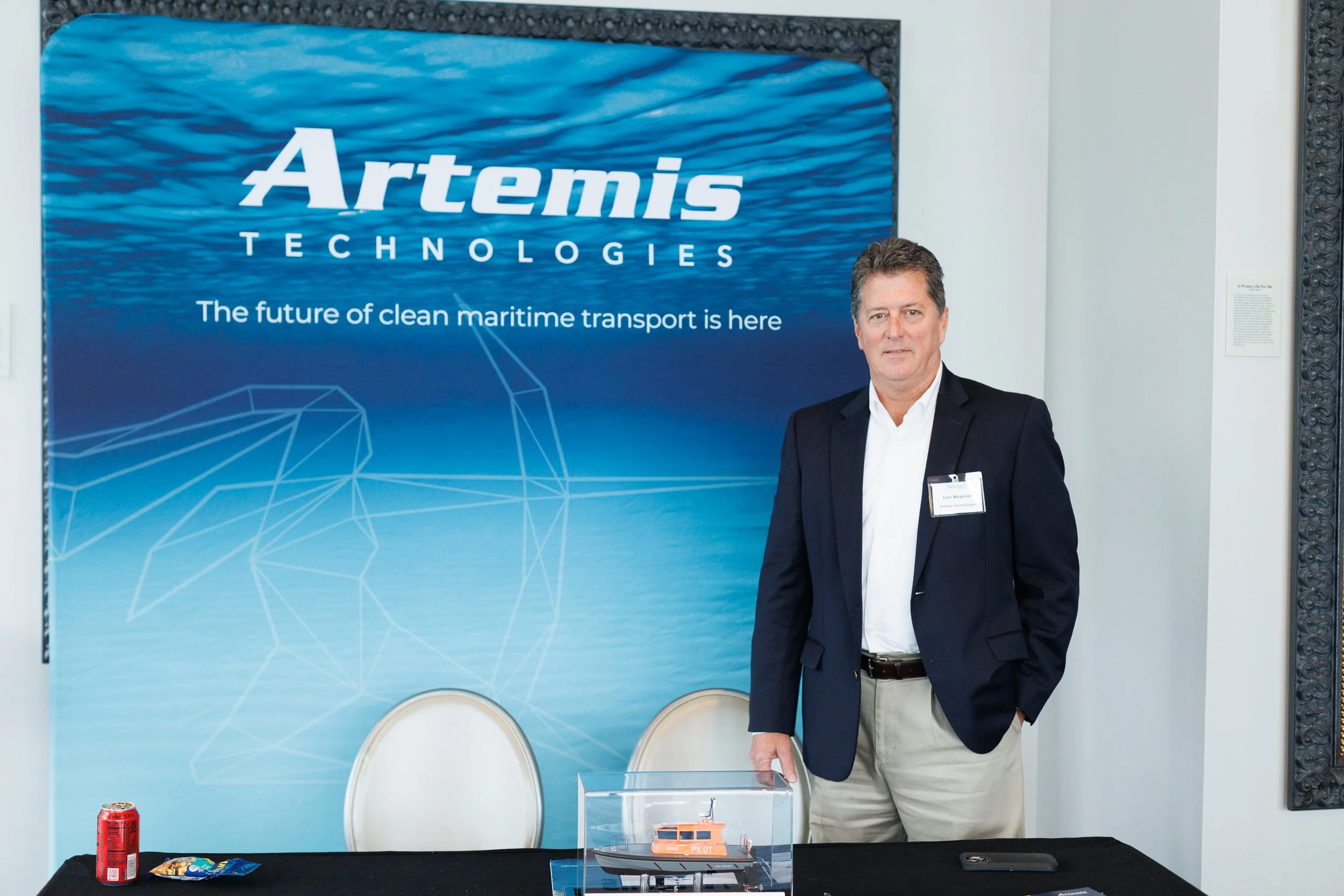 Man standing next to Artemis Technologies promotional display with a small model boat on the table in front of him.