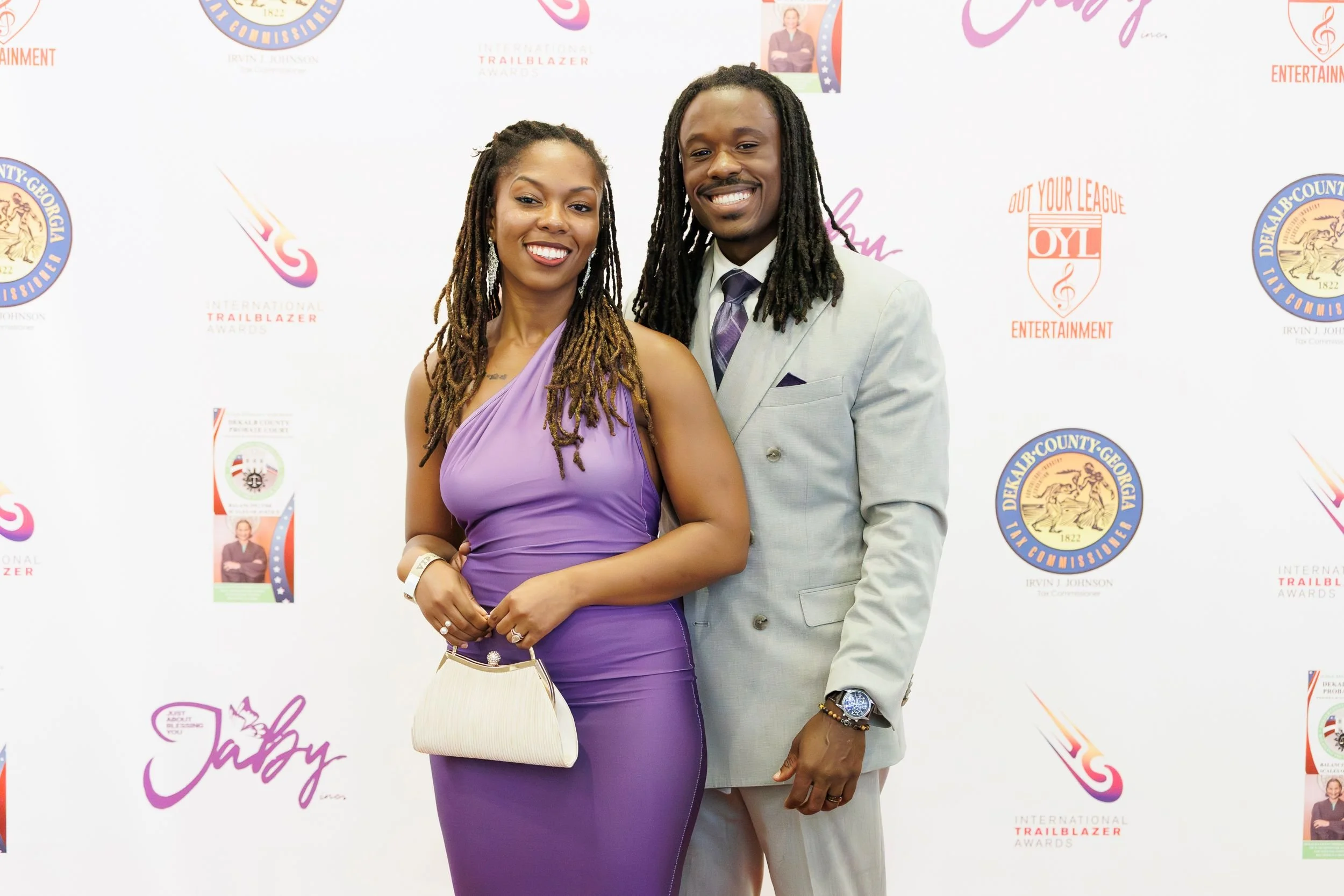 A smiling man and woman in formal attire posing together on a step-and-repeat backdrop at an event.