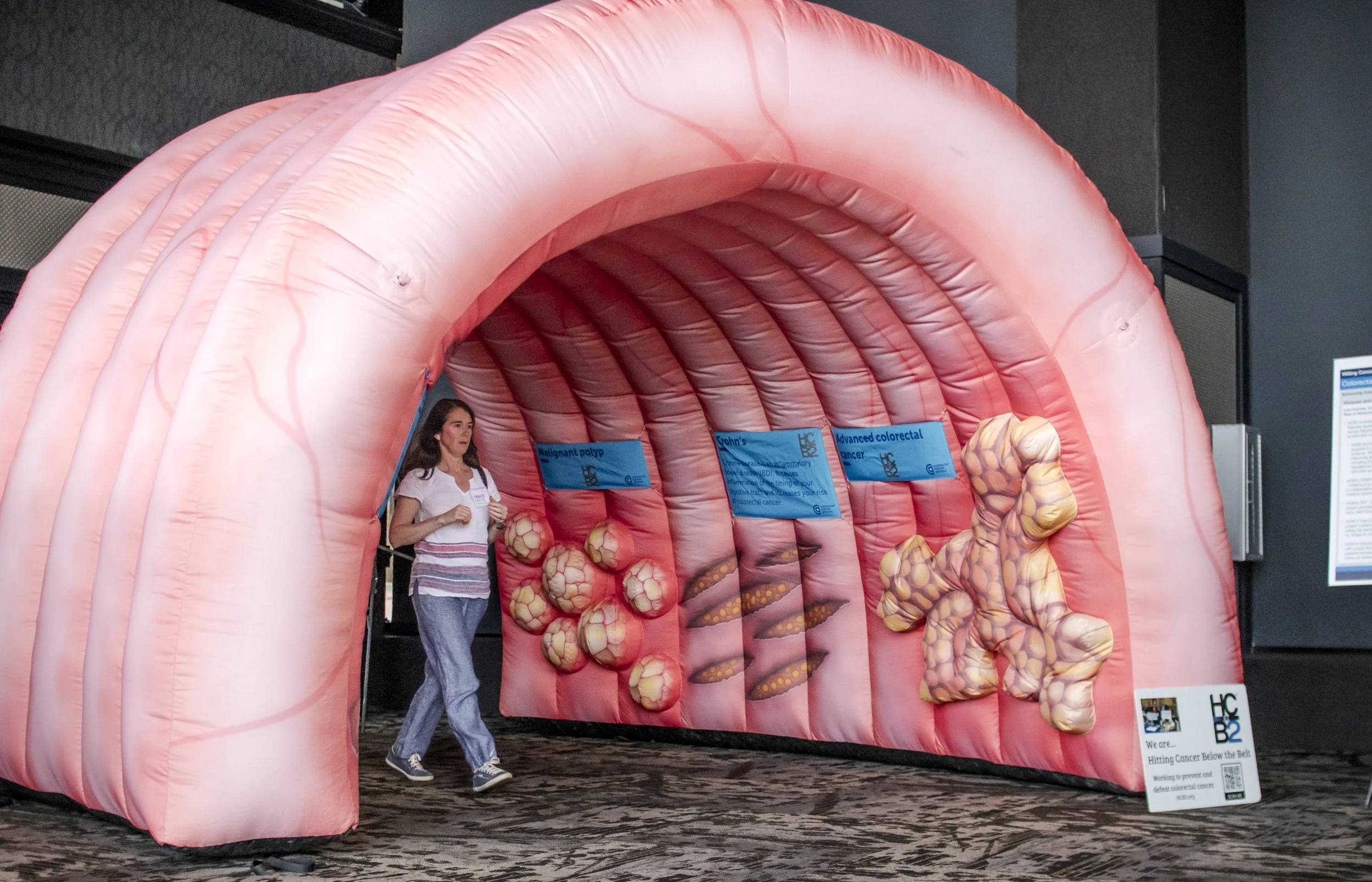 A woman walking through an inflatable anatomy exhibit representing the large intestine and colorectal cancer, with informational signs about different colorectal conditions.