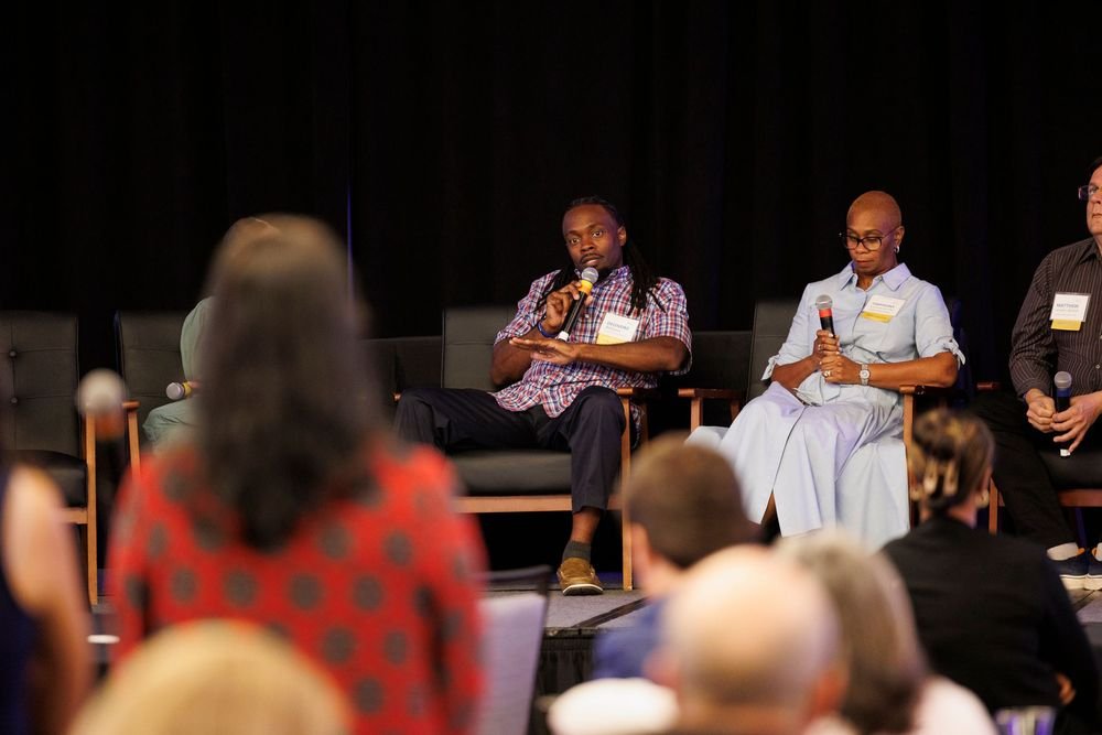 Panel discussion at a conference with three speakers sitting on stage holding microphones, engaging with an audience.