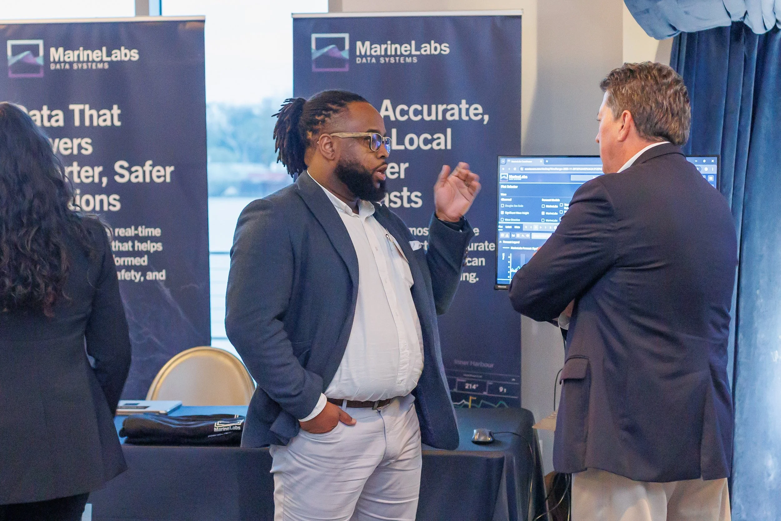 Two men having a discussion at a conference booth with banners in the background displaying 'MarineLabs' and information about data systems and solutions.