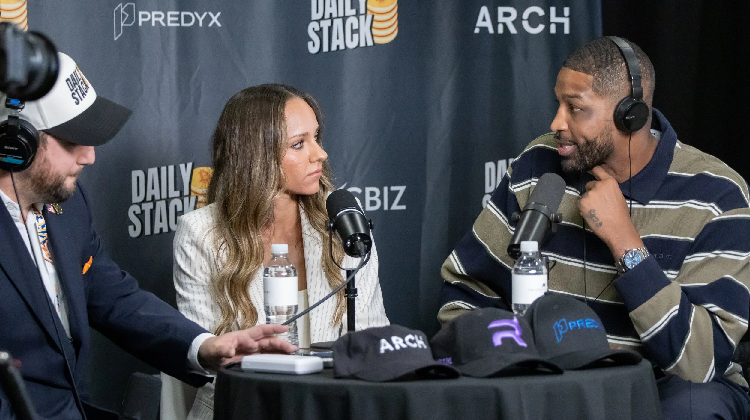 Four people sitting at a table during a podcast interview, with a black backdrop featuring the logos 'PredyX,' 'Daily Stack,' and 'Arch.' There are microphones and water bottles on the table.