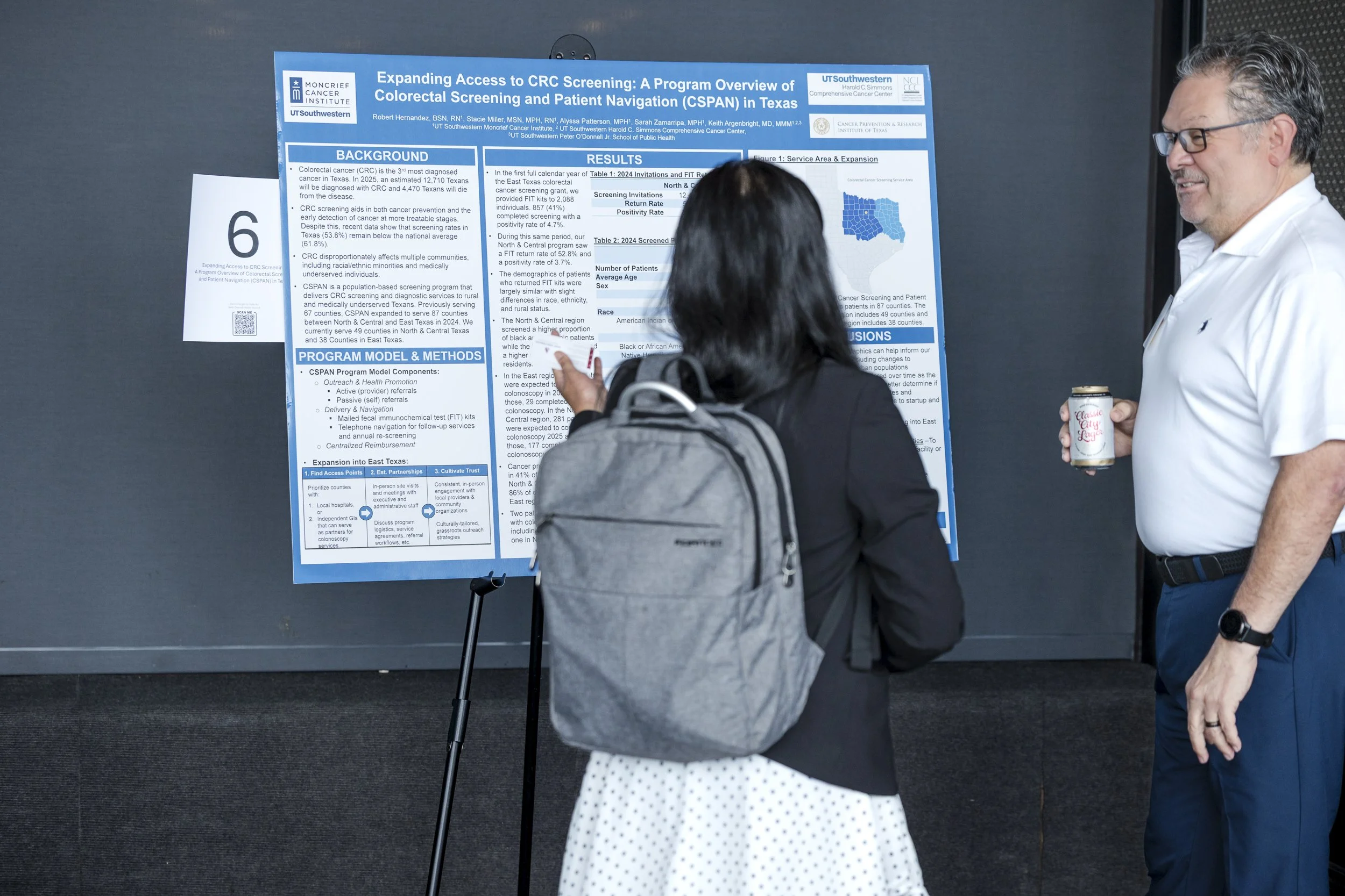 Two people standing in front of a scientific research poster at a conference. One person is pointing at the poster while the other holds a drink. The poster discusses expanding access to colorectal cancer screening in Texas.