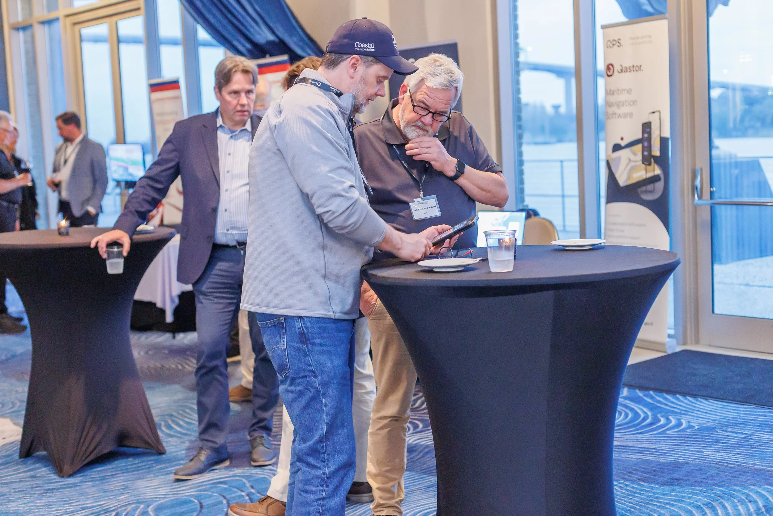 Three men standing around a tall table at a conference, looking at a phone.
