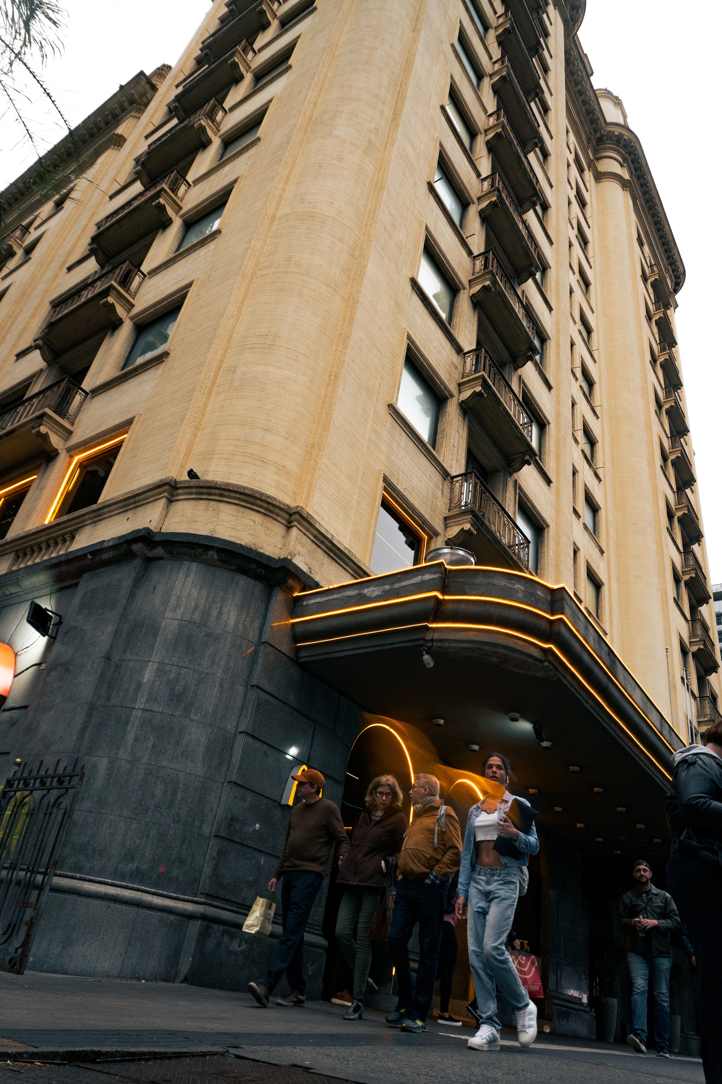 Prédio alto com detalhes em decoração na fachada e pessoas caminhando na calçada na frente.