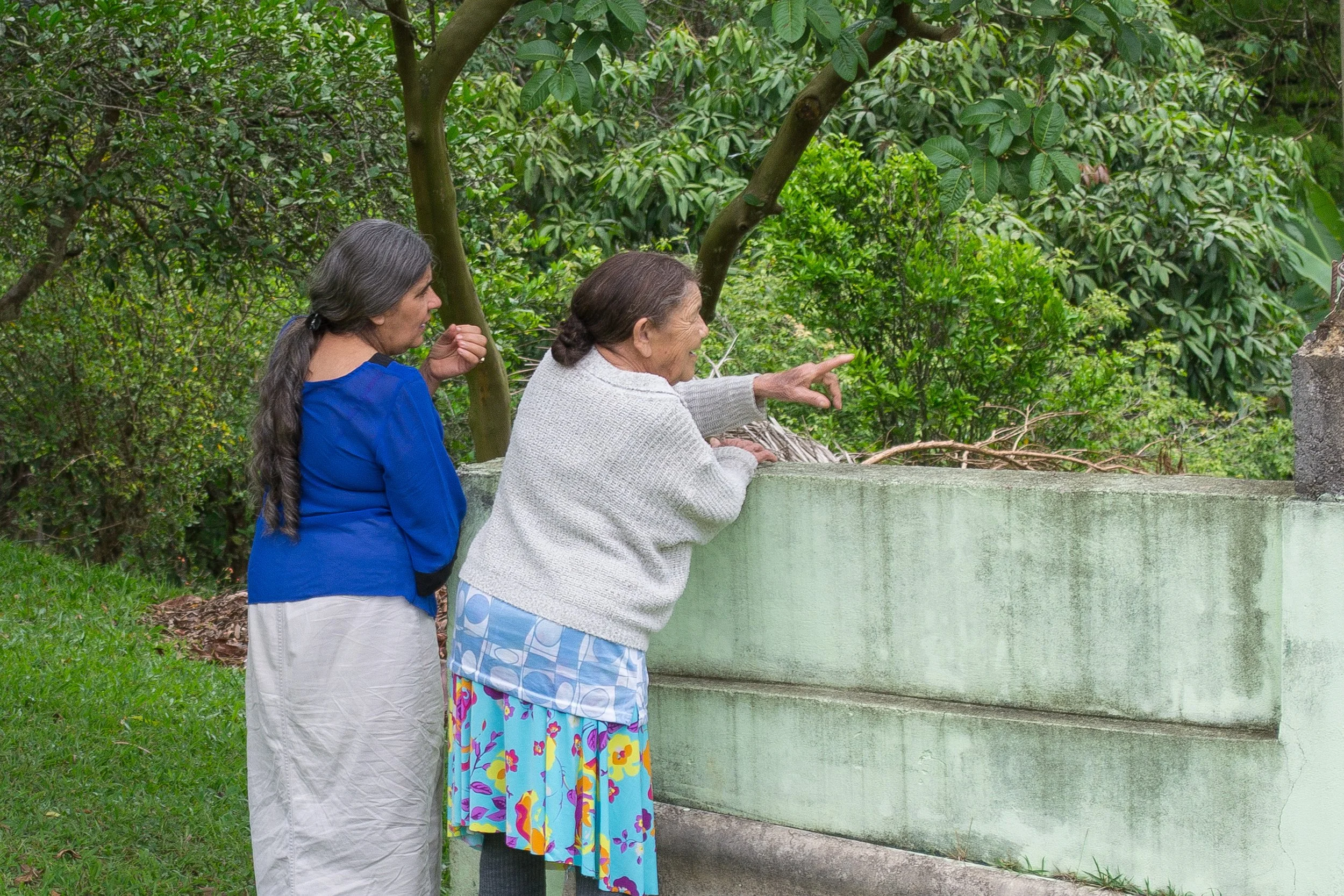 Duas mulheres idosas observando um urso de perto em uma área ao ar livre, com árvores e vegetação ao fundo.