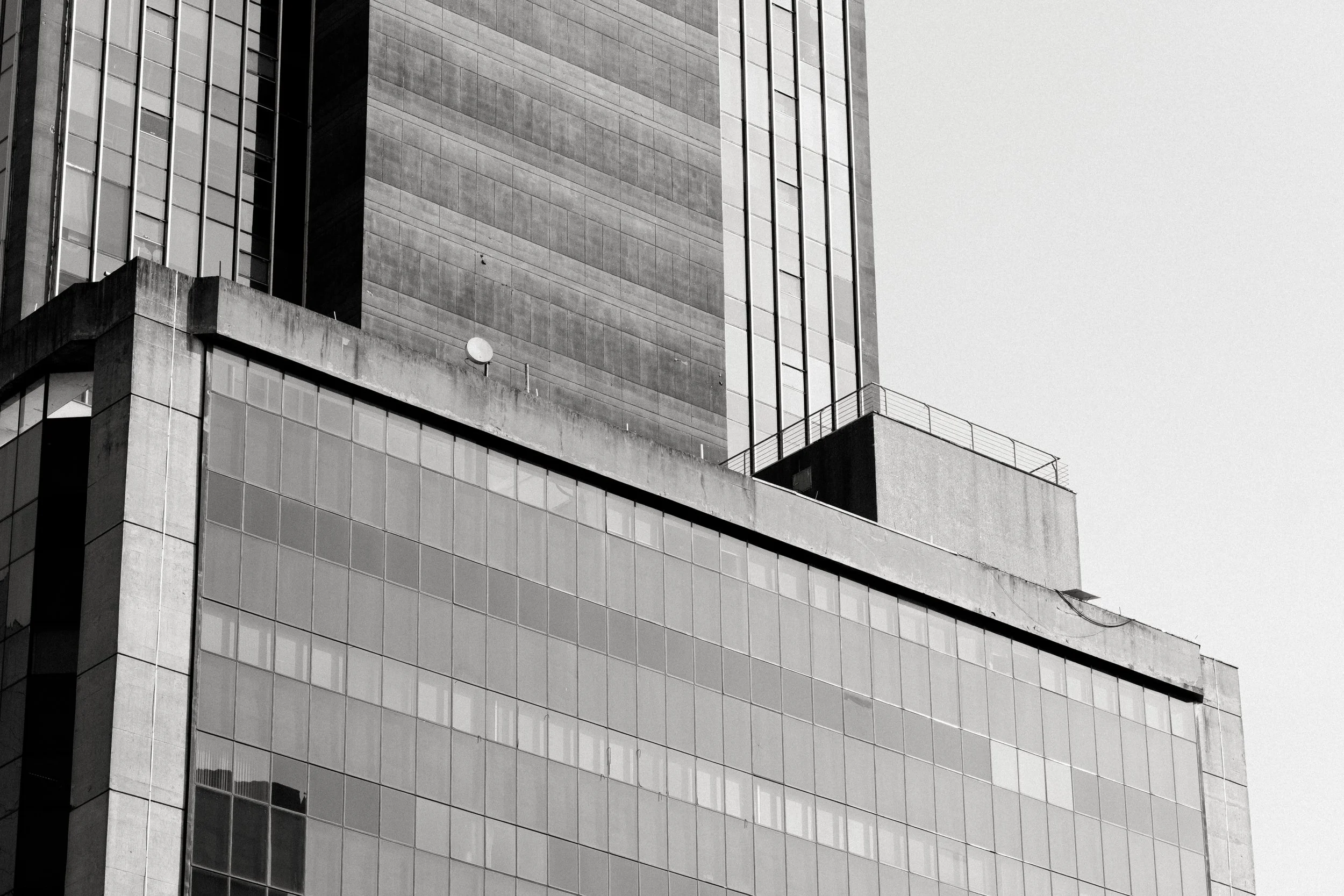 Imagem em preto e branco de um arranha-céu de perfil, com várias janelas de vidro refletindo a luz, destacando sua estrutura moderna e multifacetada.
