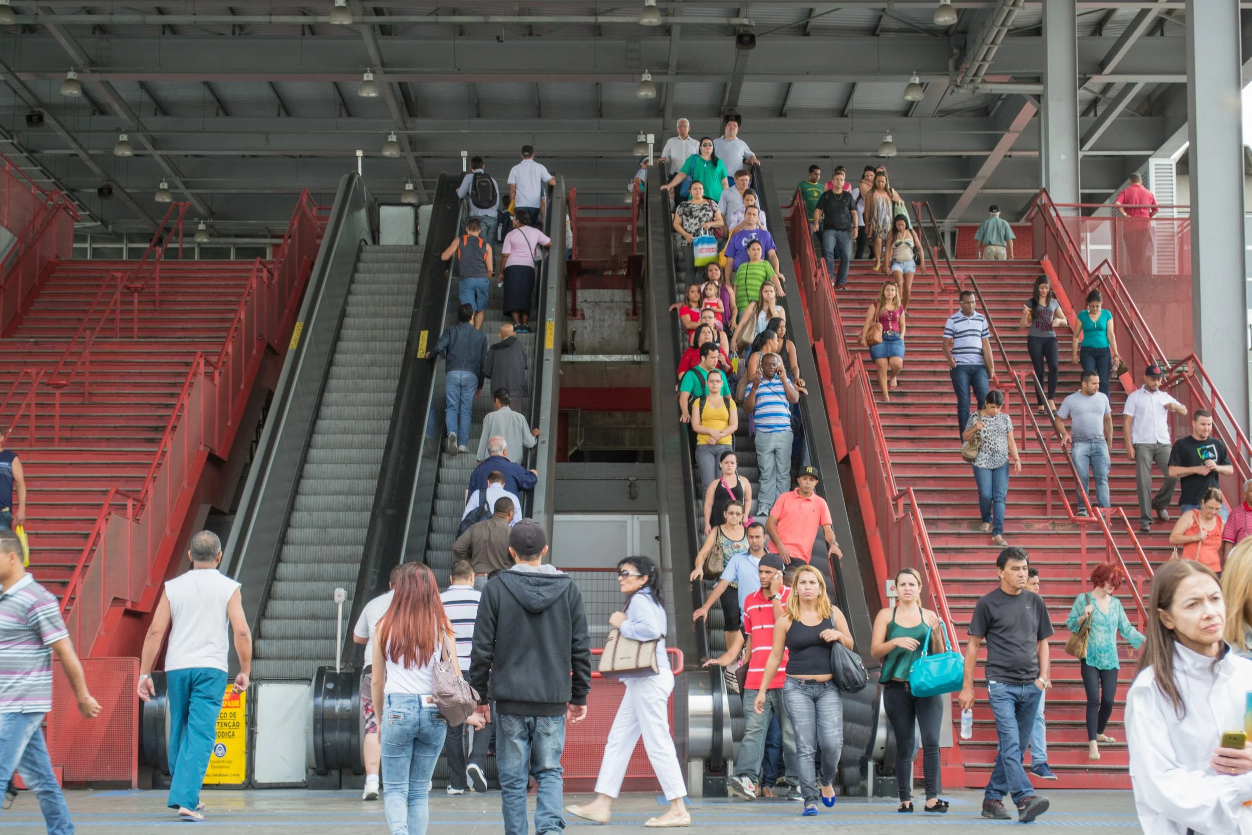 Imagem de uma estação de metrô com escadas e escadas rolantes lotadas de pessoas.