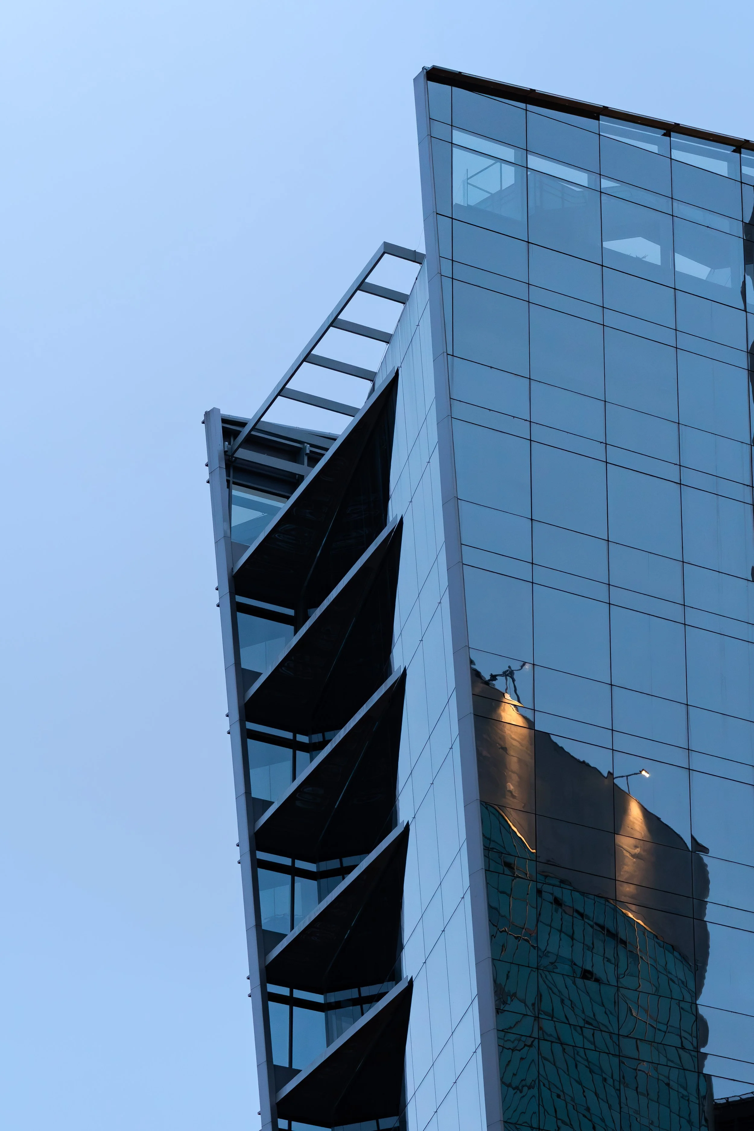 Fachada de um edifício moderno de vidro refletindo o céu e outros edifícios ao redor.