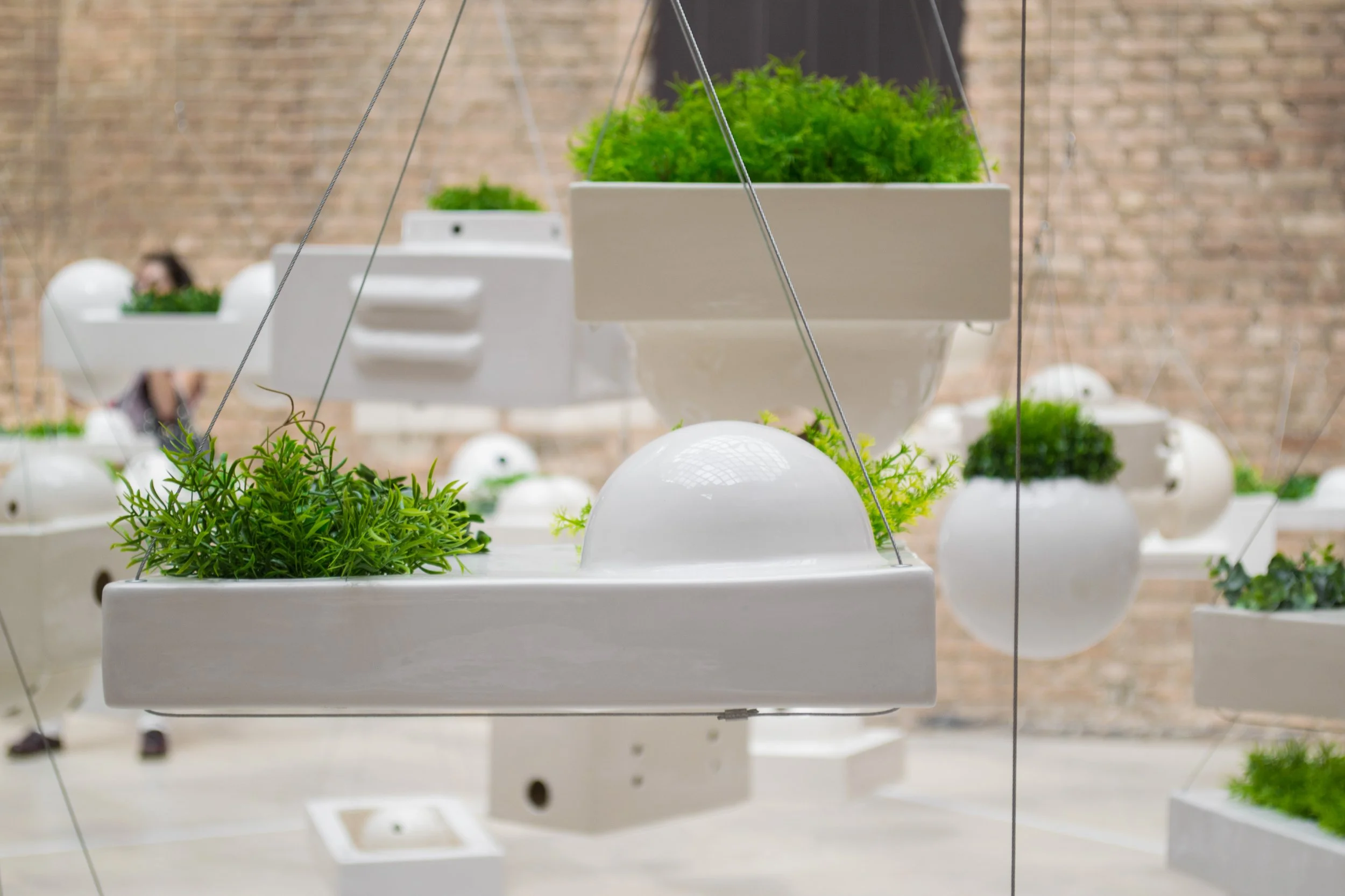 Vasos suspensos brancos com plantas verdes em uma parede de fundo de tijolos.