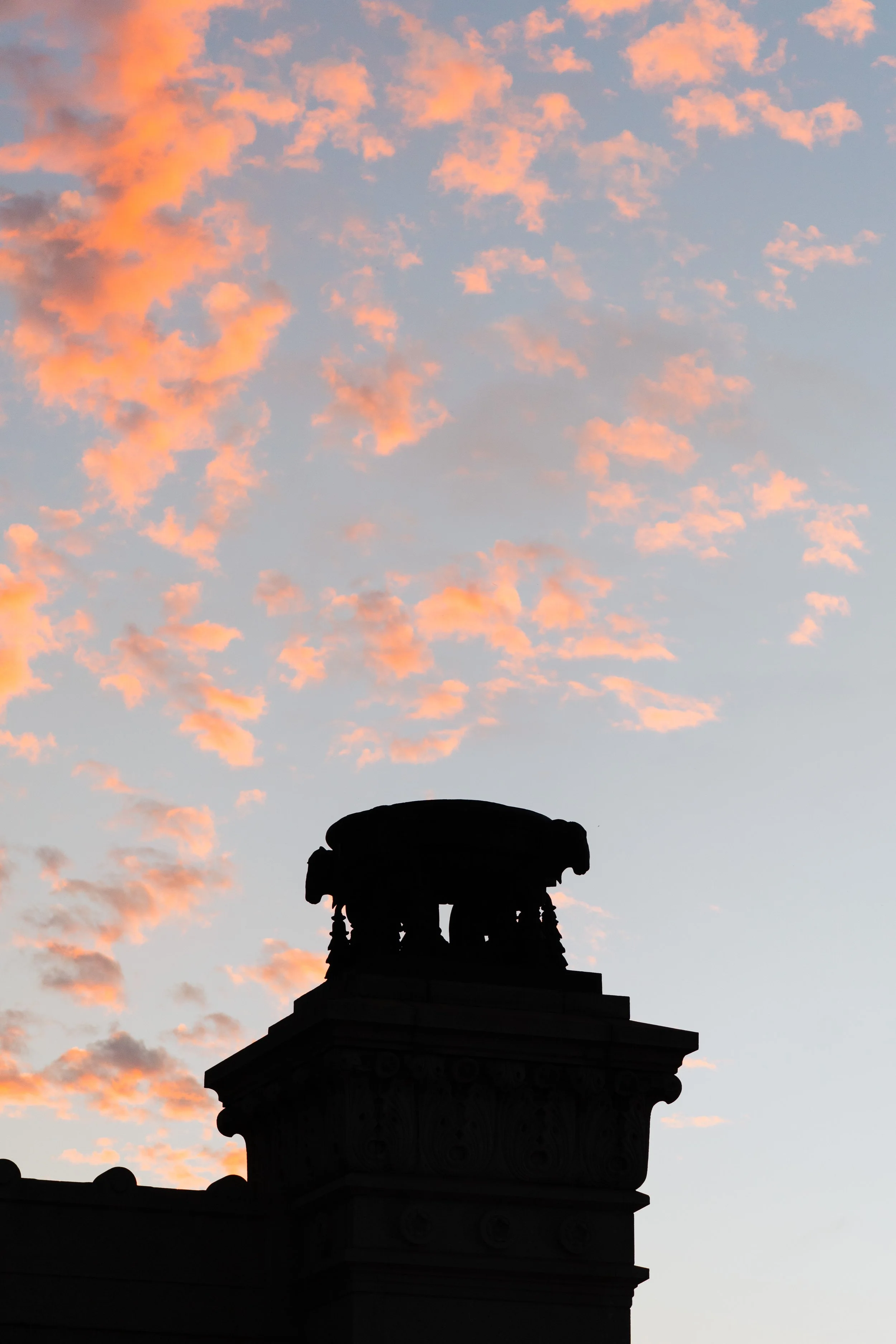 Silhueta de uma estrutura arquitetônica no pôr do sol com nuvens cor de rosa no céu.