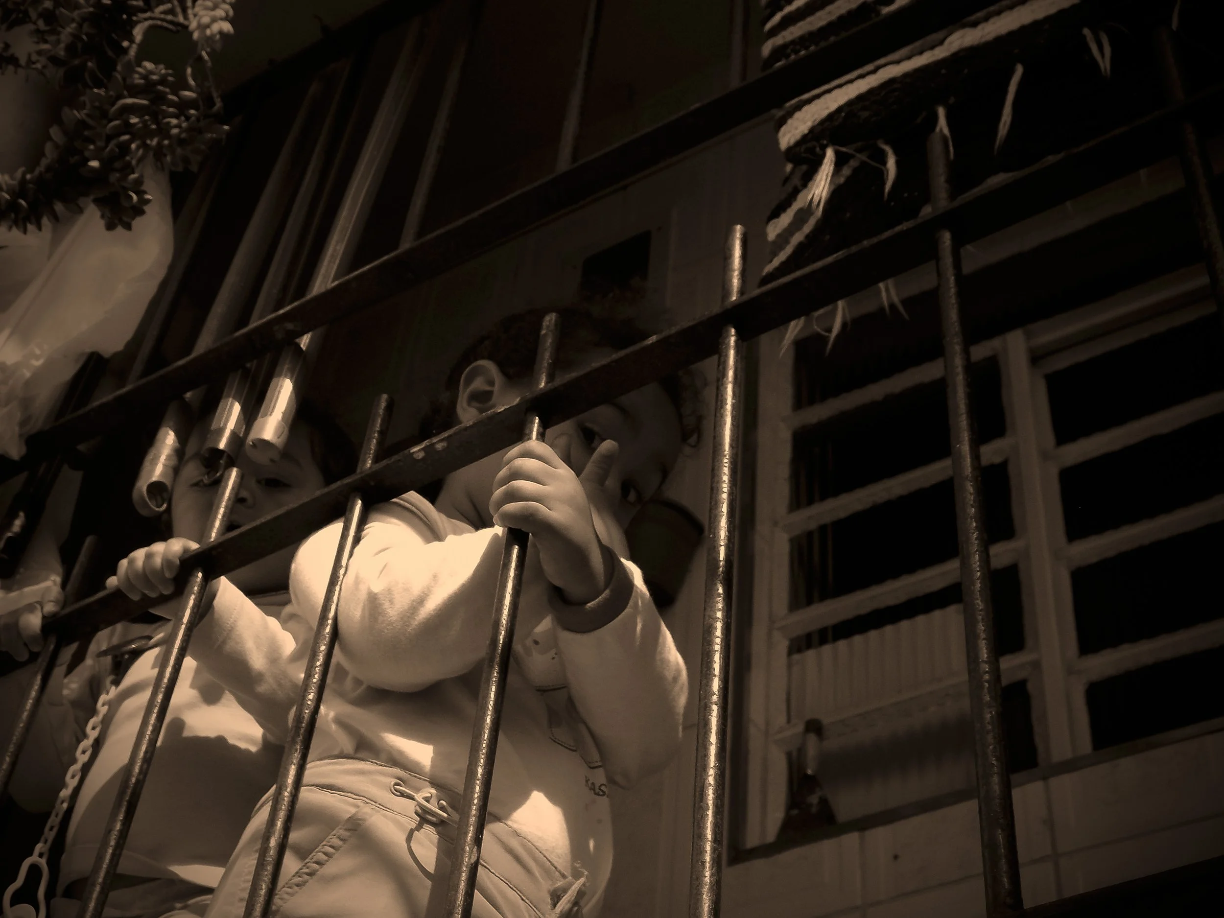 Crianças atrás de grades em um ambiente interno com uma janela ao fundo.