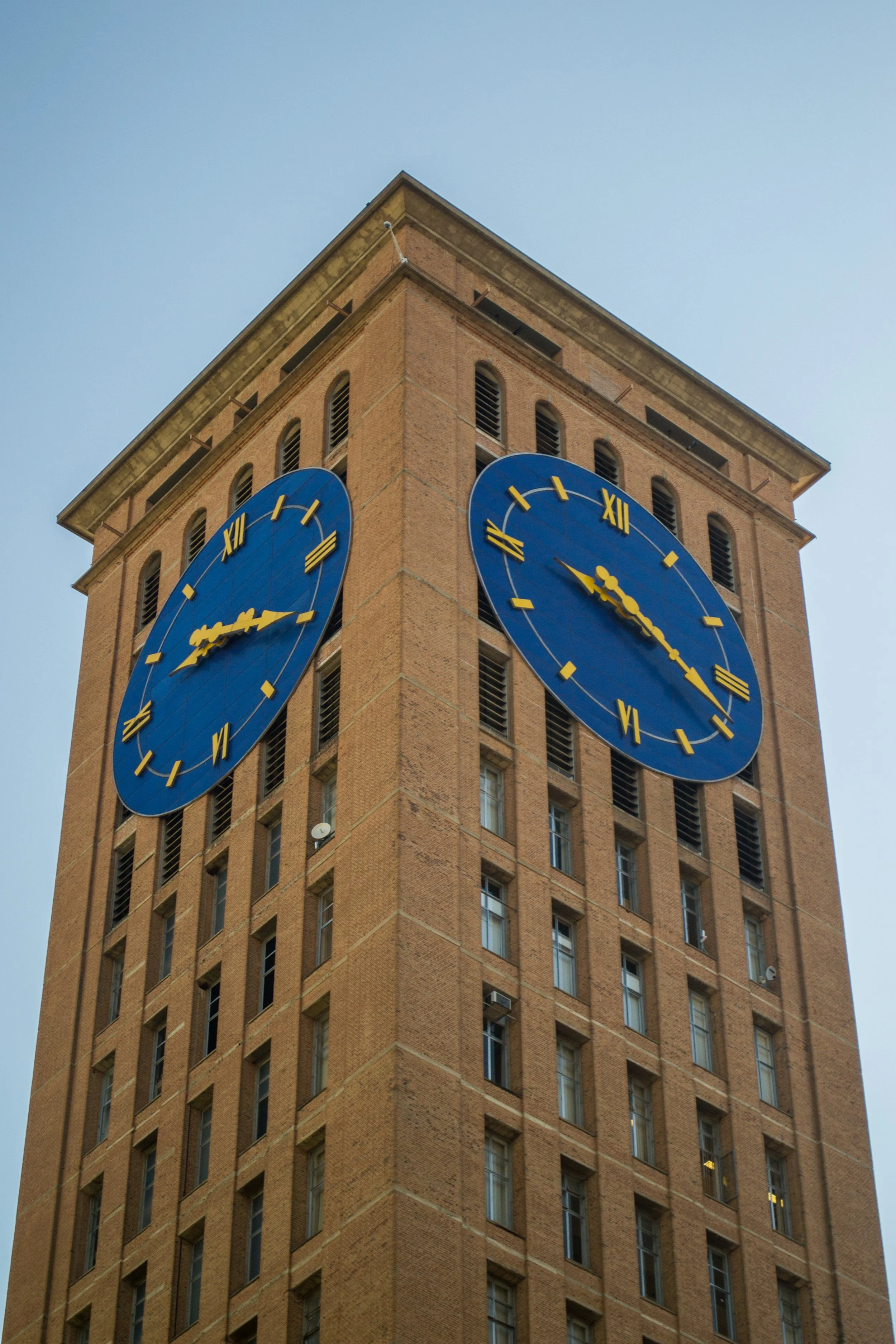 Relógio de torre de um prédio alto, com fundo de céu claro.