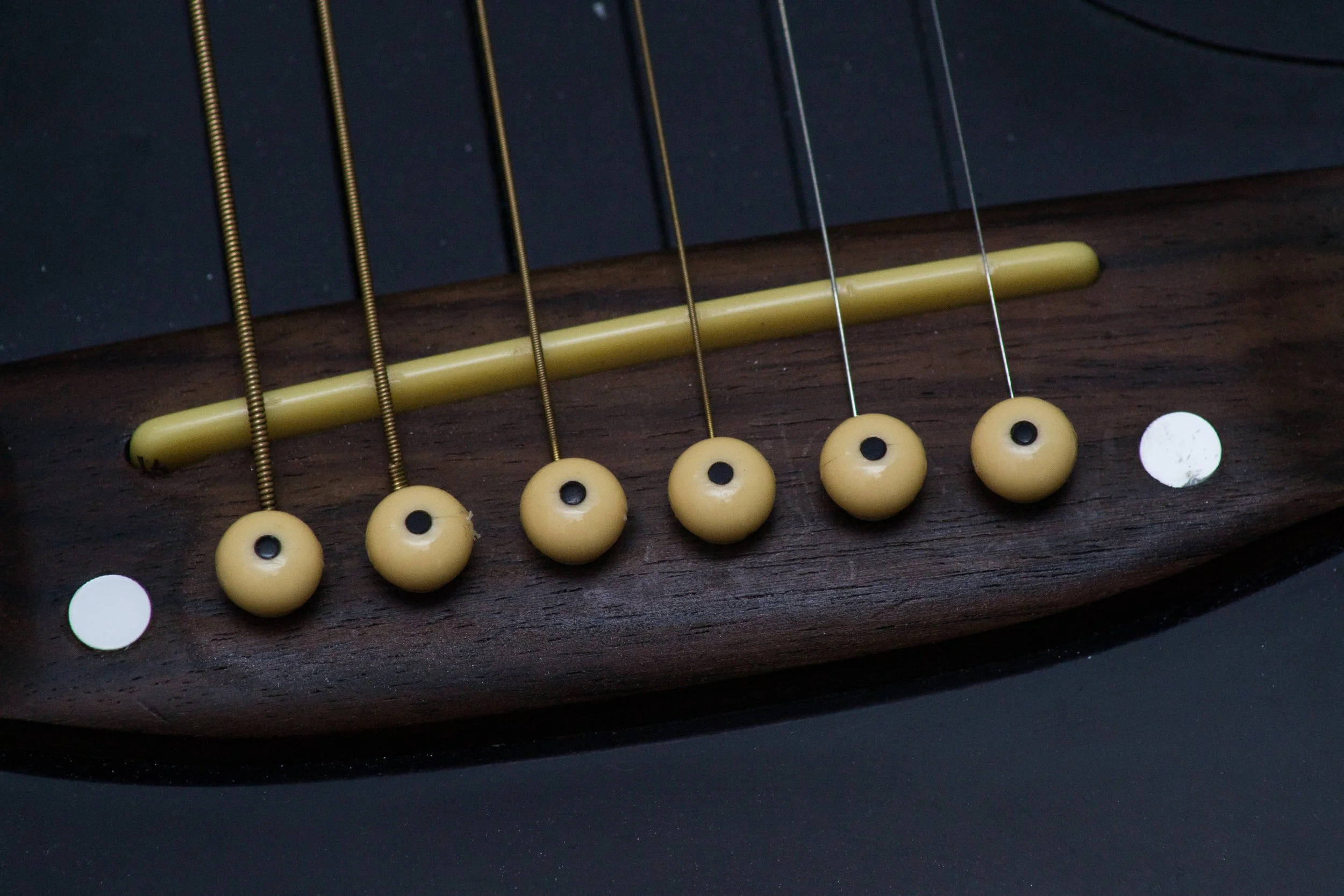 Detalhe de uma corda de violão, mostrada de perto, com a madeira escura do corpo do instrumento e as caixas brancas e componentes internos das cordas visíveis.