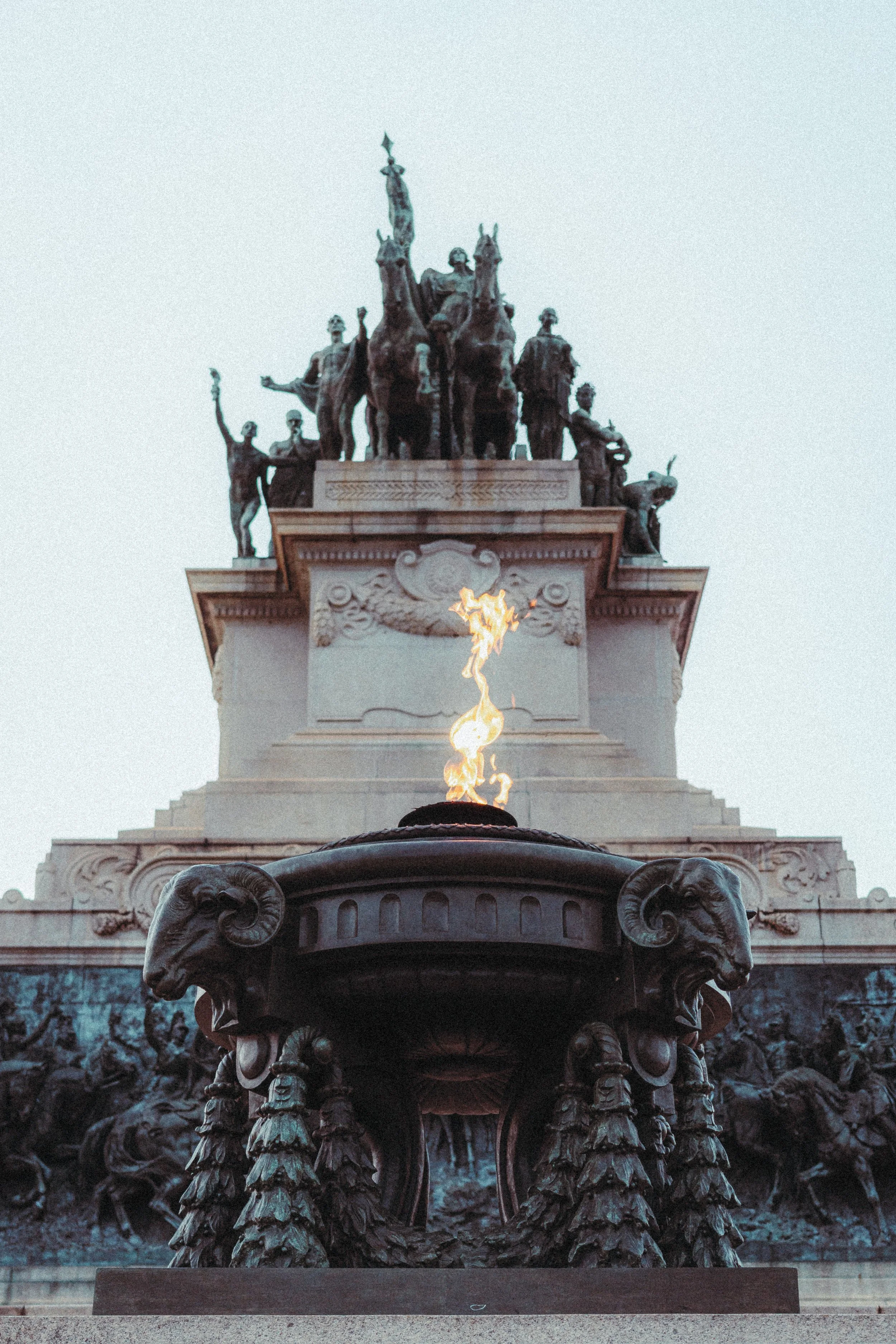Monumento com uma fogueira preciosa na frente e escultura de figuras humanas e animais na parte superior.