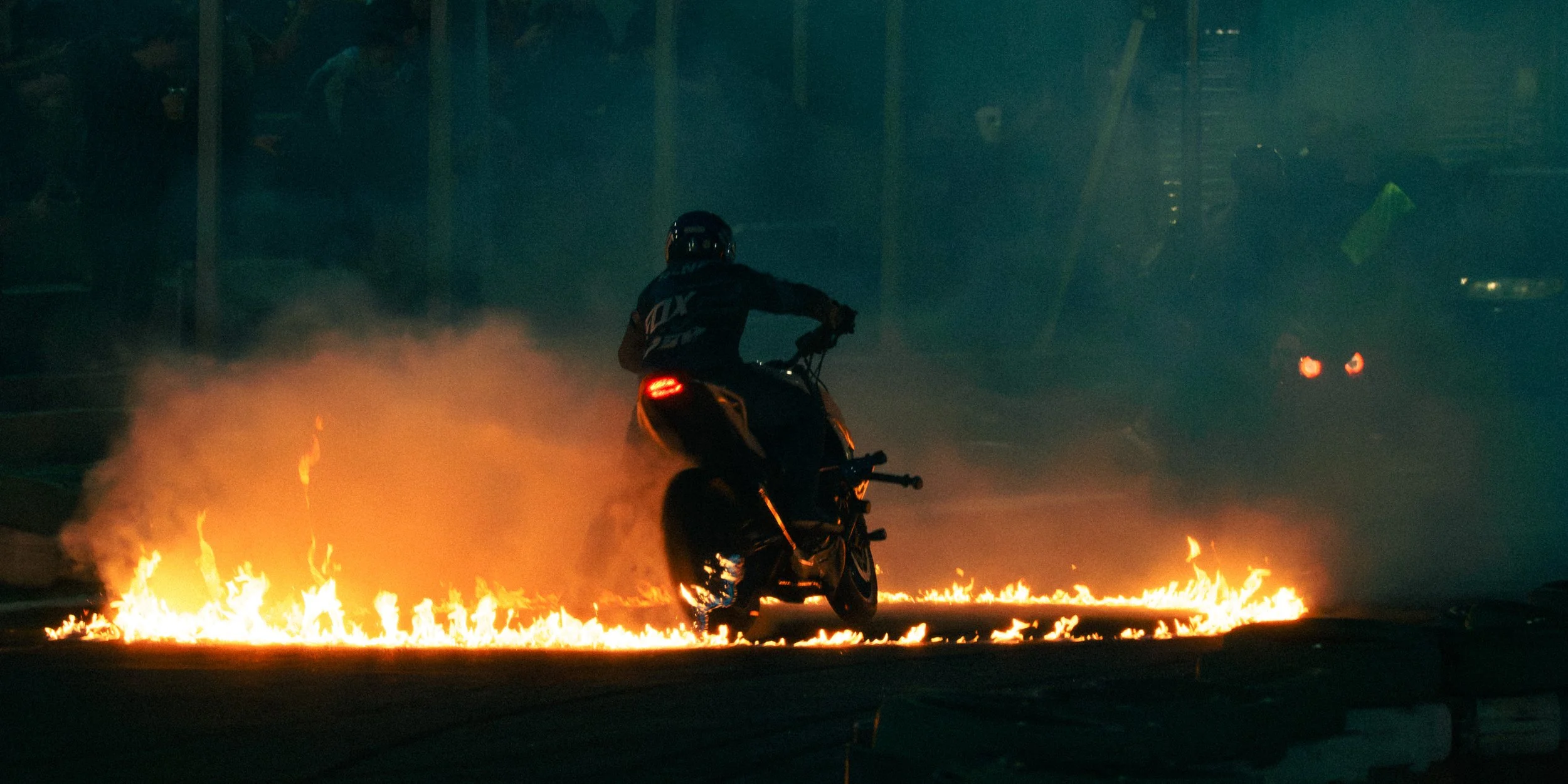 Motociclista passando sobre uma faixa de fogo na rua durante a noite.