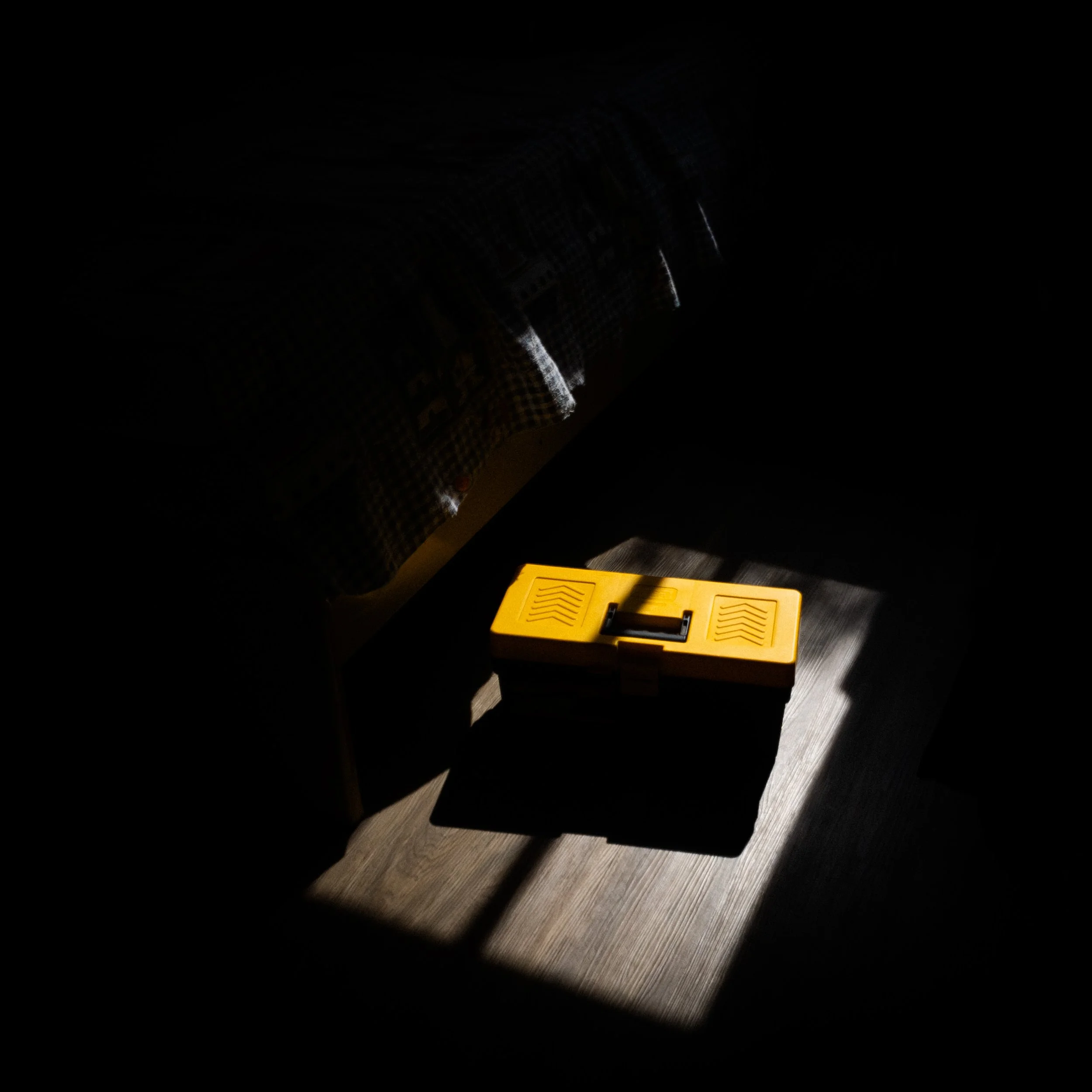 Caixa amarela de ferramentas sob iluminação suave no canto de um espaço escuro, com luz incidindo parcialmente, criando sombra.