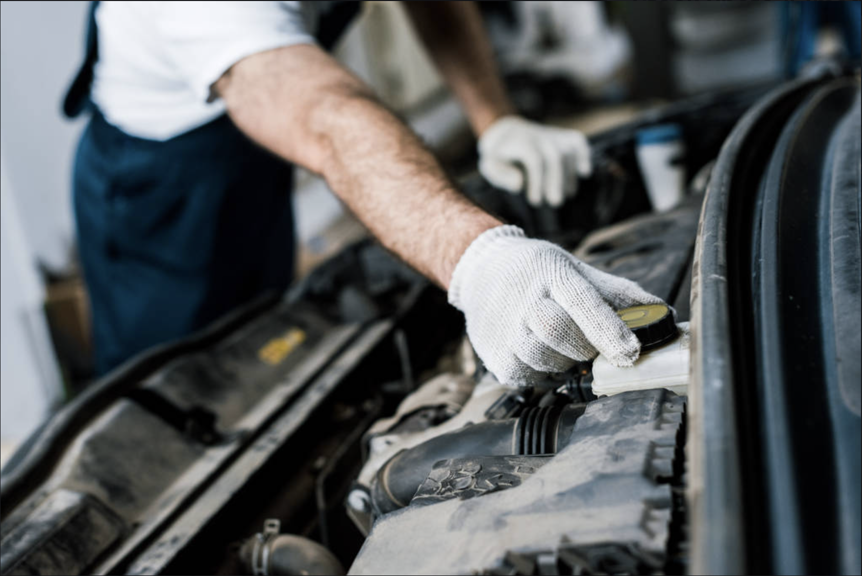 Close-up of a mechanic's arm with a white glove, using a small tool on a car engine.