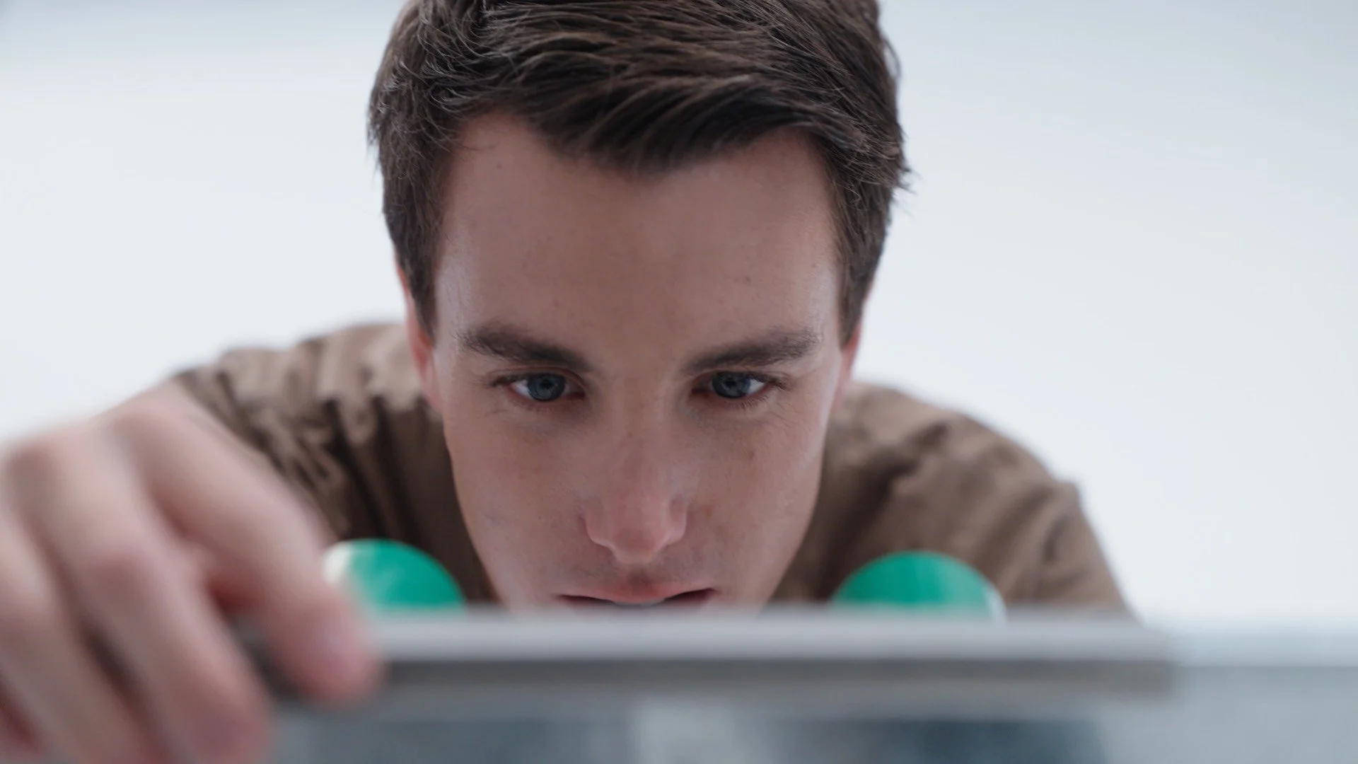 Close-up of a young man with blue eyes and dark hair, focusing intently while reaching towards the camera with his left hand, with a plain white background.