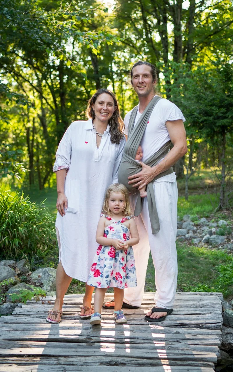 Mother and father pose with their two children on a wooden bridge outside in sunshine for family portrait session