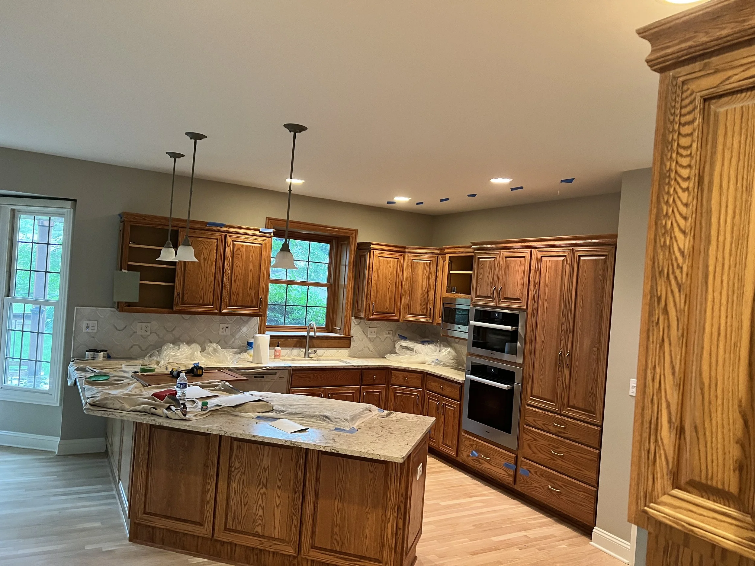 Kitchen with wooden cabinets, a central island, window above the sink, and pendant lights hanging from the ceiling, undergoing renovation.