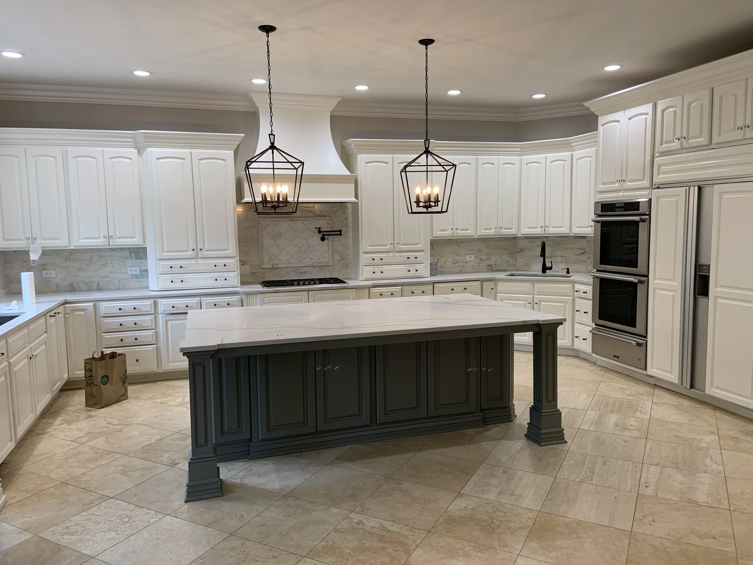 Modern spacious kitchen with white cabinetry, a central island with dark base, two pendant lights, and double ovens.